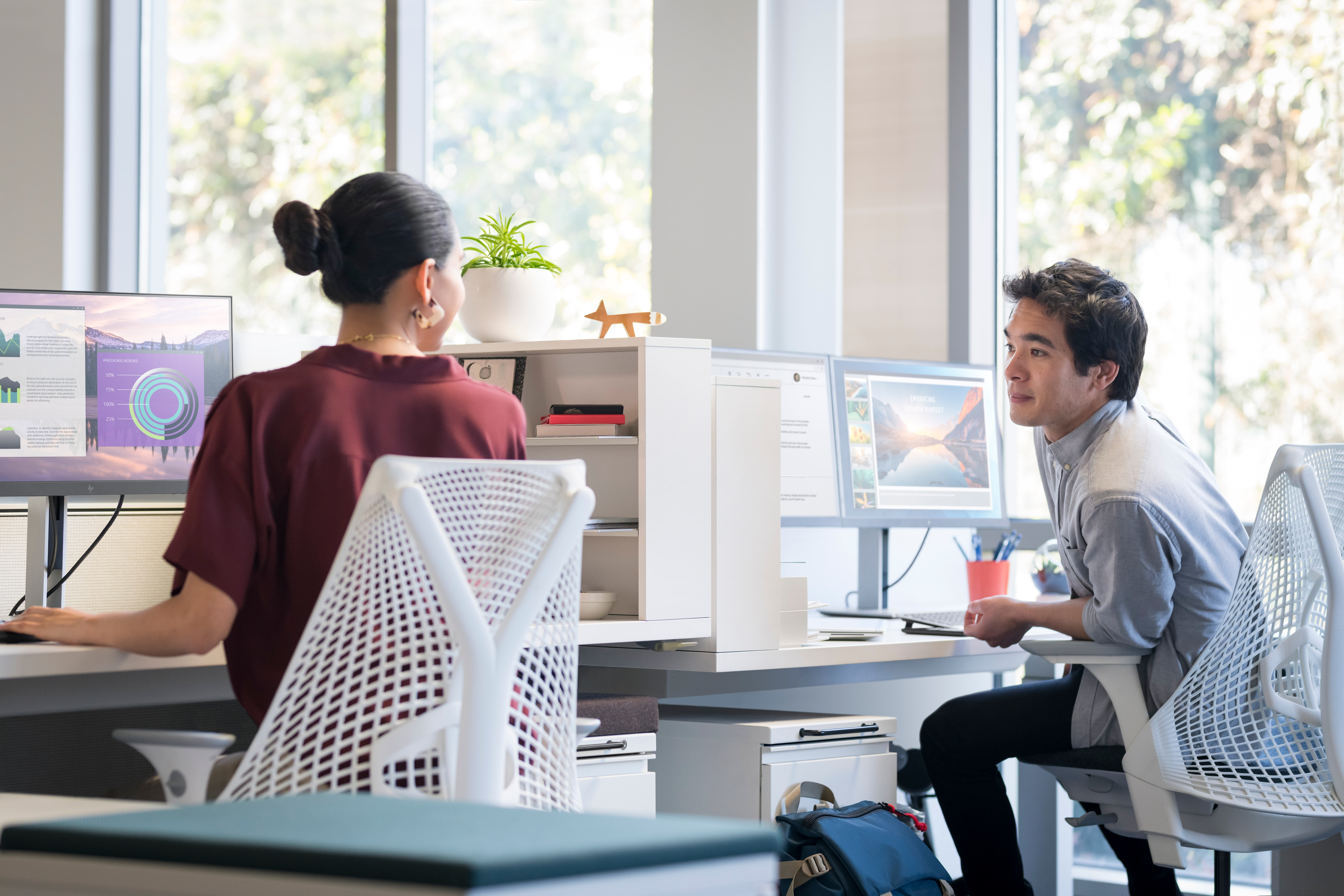 Una persona che lavora al computer con un'altra persona, in un ambiente ufficio con monitor.