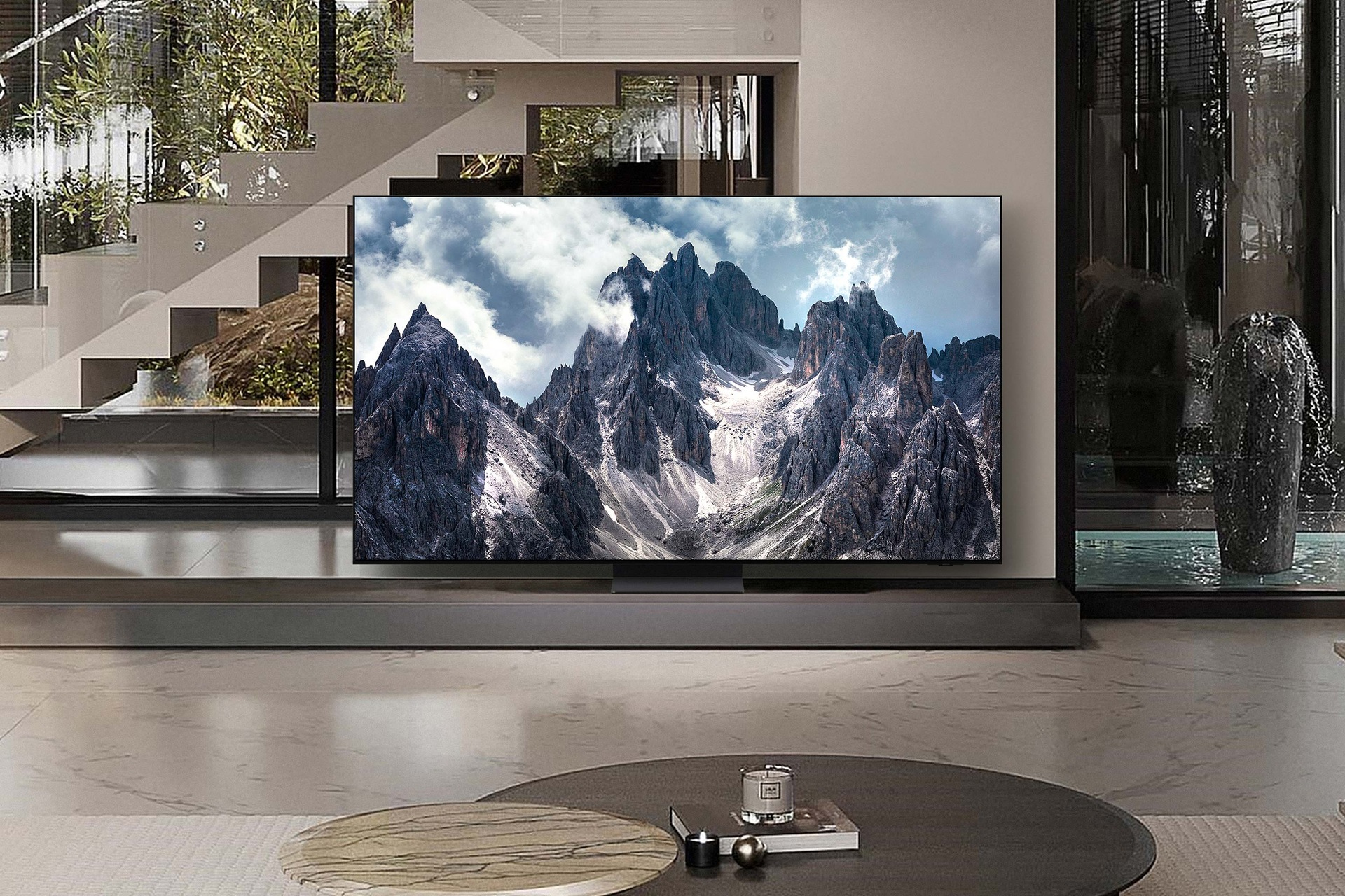 Der Fernseher zeigt eine Berglandschaft, ein Wohnzimmer mit Couchtisch und Treppe.