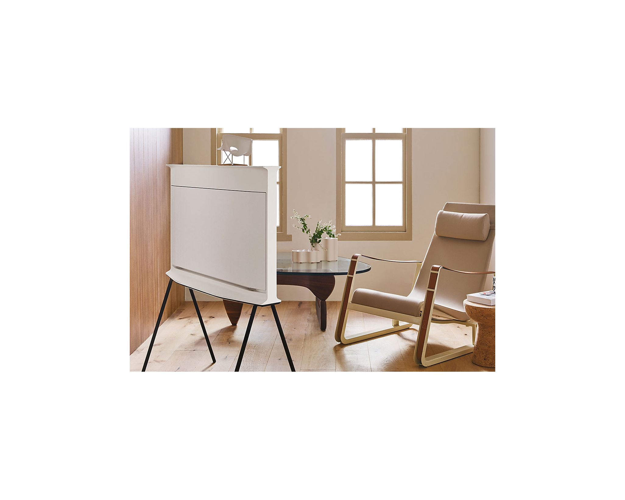 Telewizor w nowoczesnym salonie. Ma białą ramę i stoi na stojaku. Beżowe ściany.