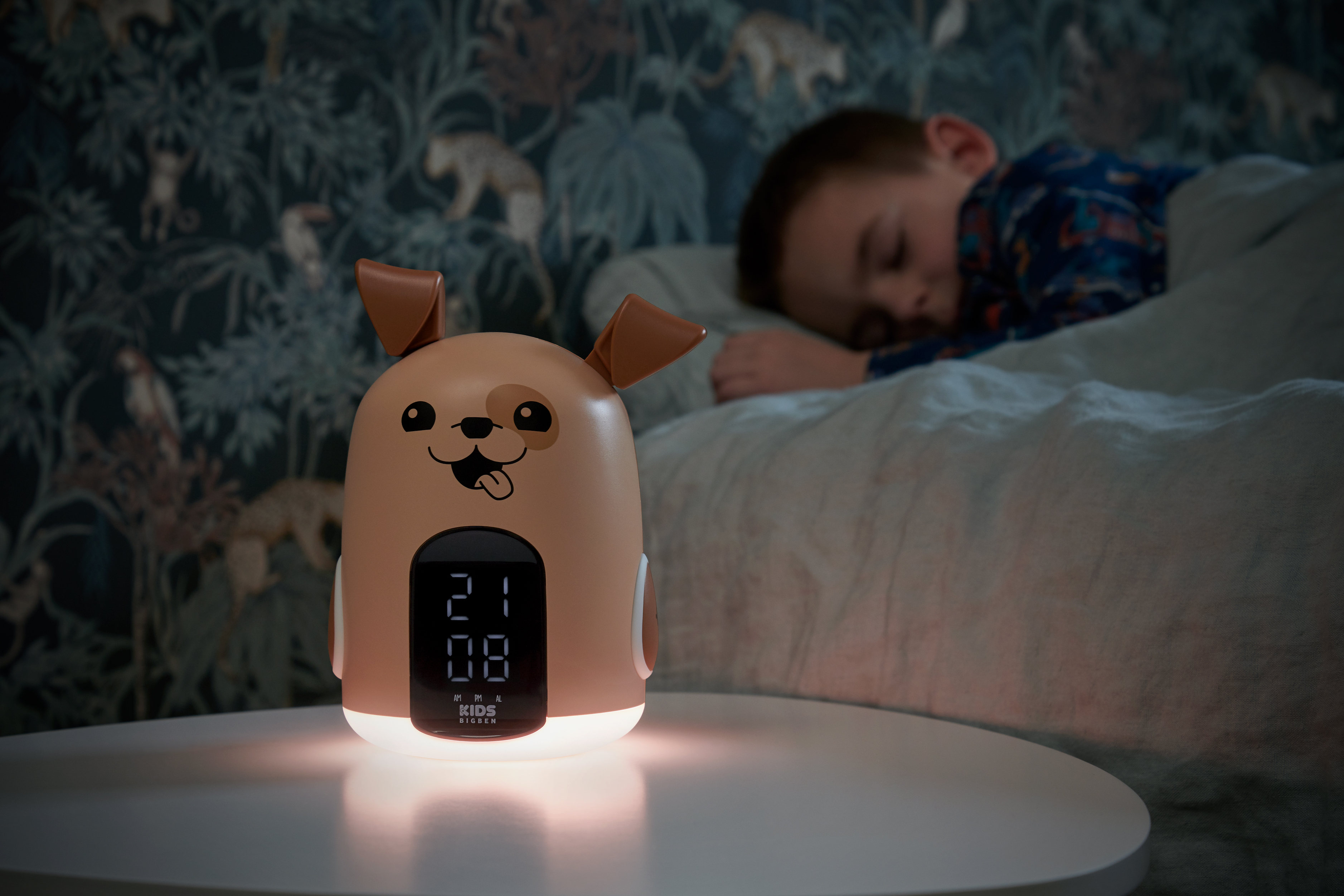 Un despertador con forma de perro brillando sobre una mesa. Un niño duerme al fondo.
