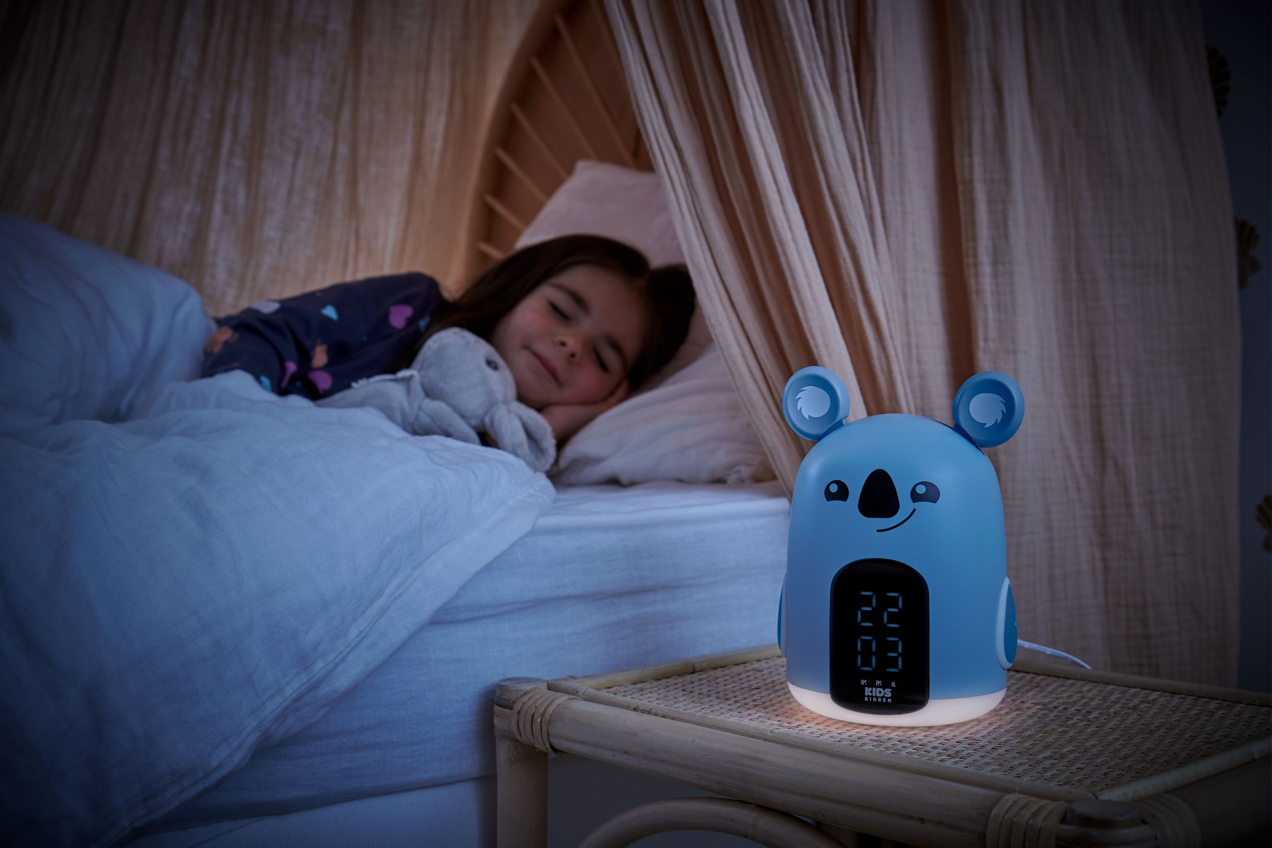 Ein Kind schläft im Bett, ein Koala-Nachtlicht mit der Uhrzeit auf einem Nachttisch.