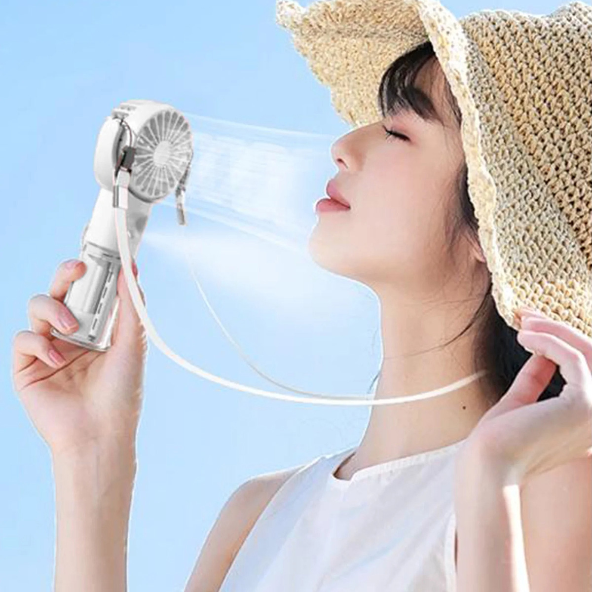 Mujer usando un ventilador de mano, rociando niebla. Lleva sombrero, cielo azul de fondo.