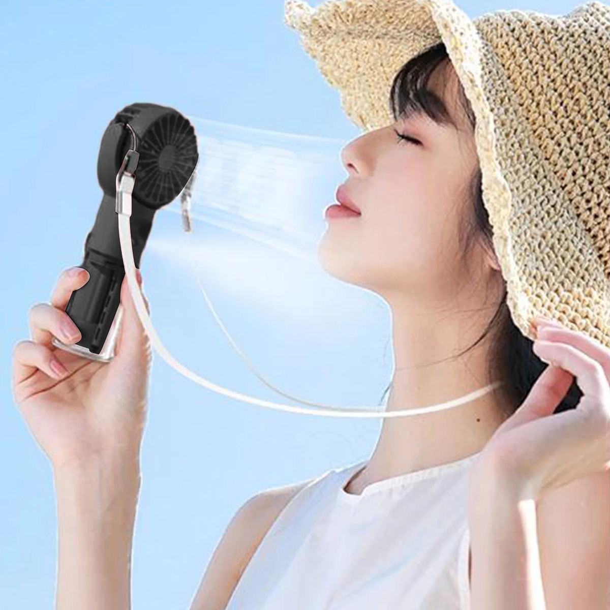 Una donna usa un ventilatore portatile nero, con una cinghia, su sfondo di cielo blu.