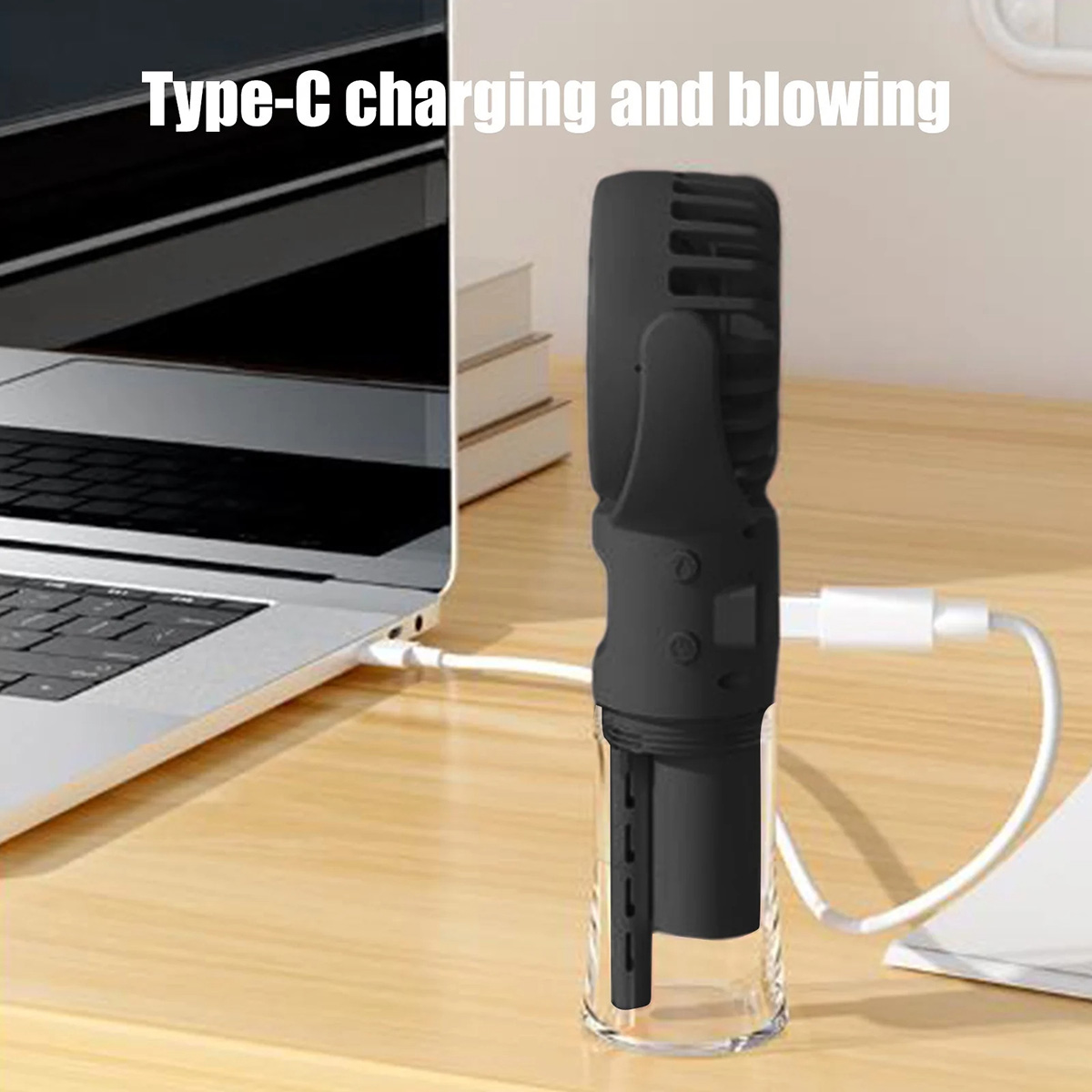 Un ventilatore portatile nero si carica tramite un cavo USB-C accanto a un laptop.