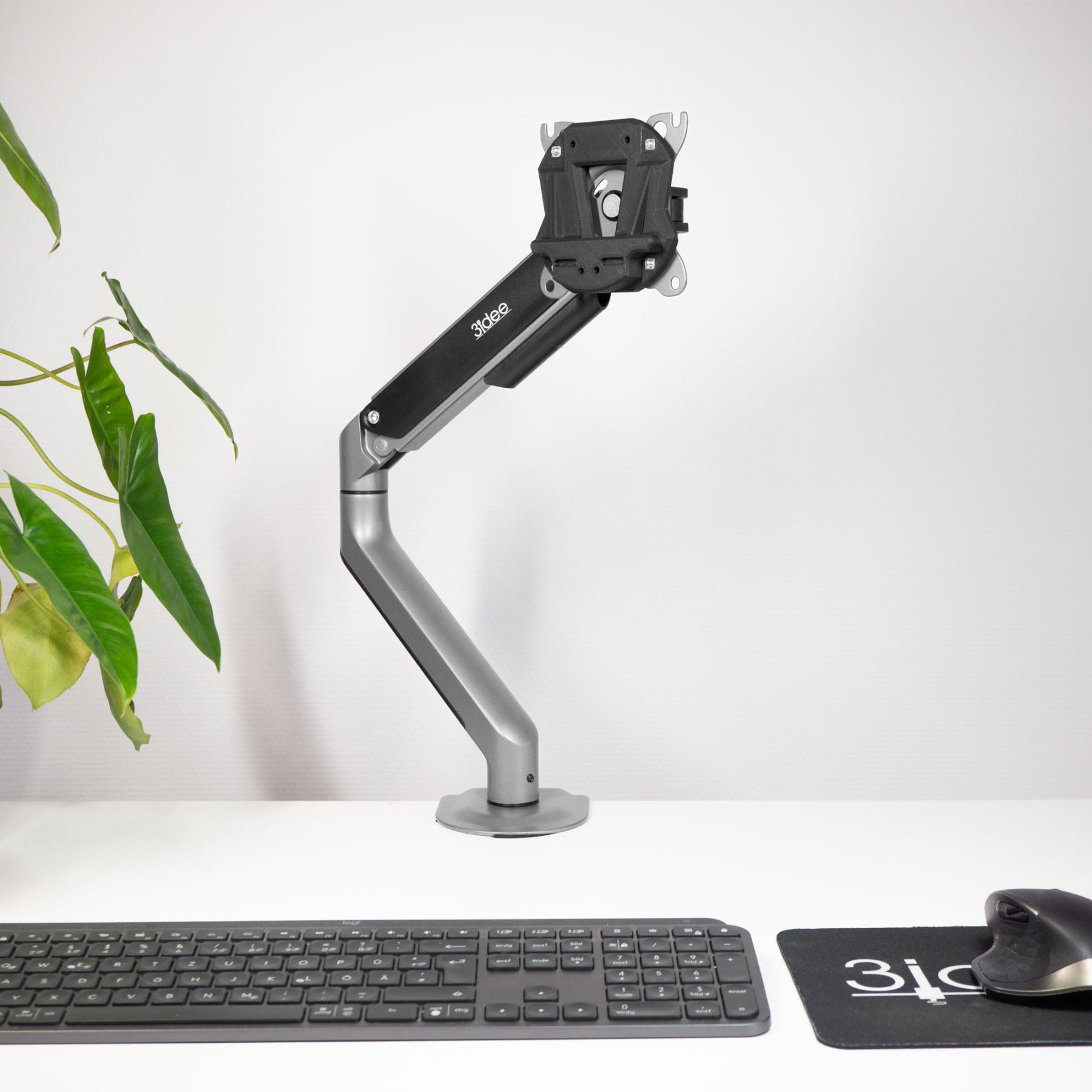 Monitorarm mit an einer weißen Wand befestigtem Monitor. Tastatur, Maus und Schreibtisch sind ebenfalls sichtbar.