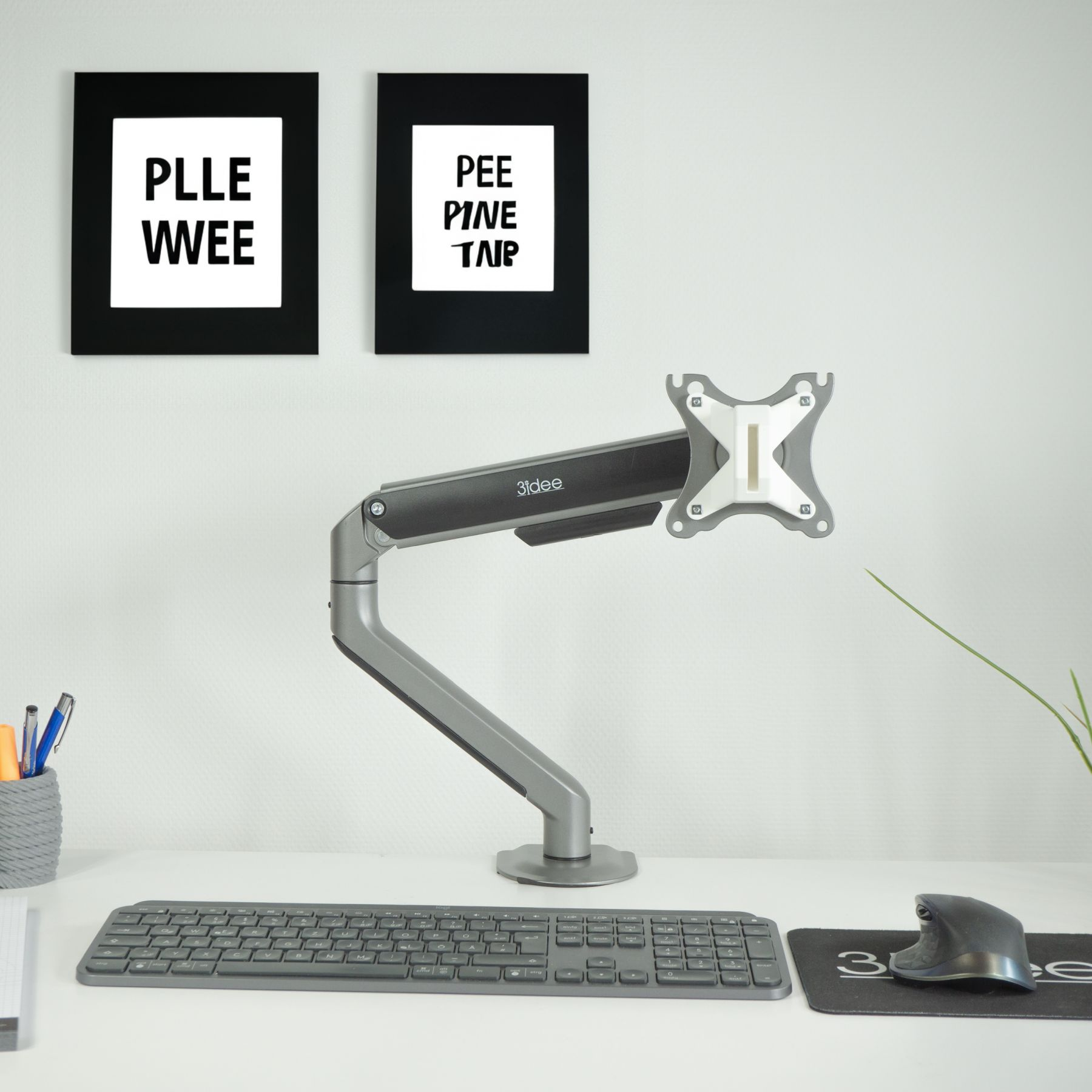 Schreibtischaufbau mit Monitorarm, Tastatur, Maus und zwei gerahmten Drucken.