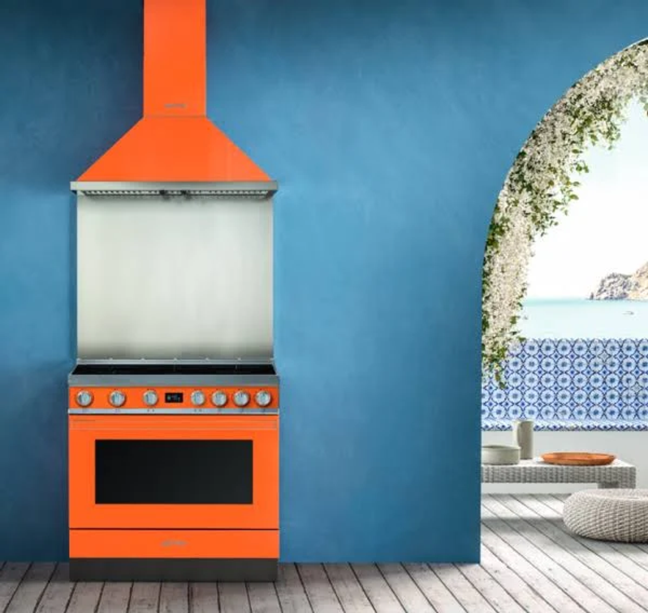 Cucina arancione con fornello, cappa e parete blu. Un arco conduce a una vista esterna.