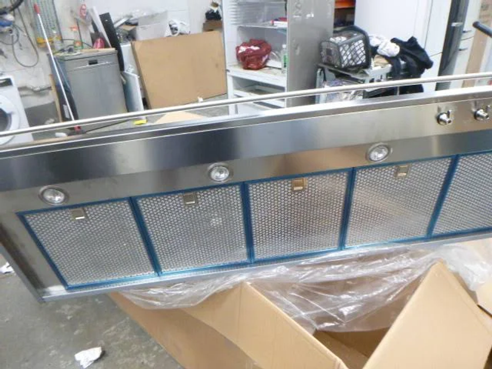 Campana extractora de acero inoxidable con cinco filtros de malla metálica, dentro de una caja de cartón.