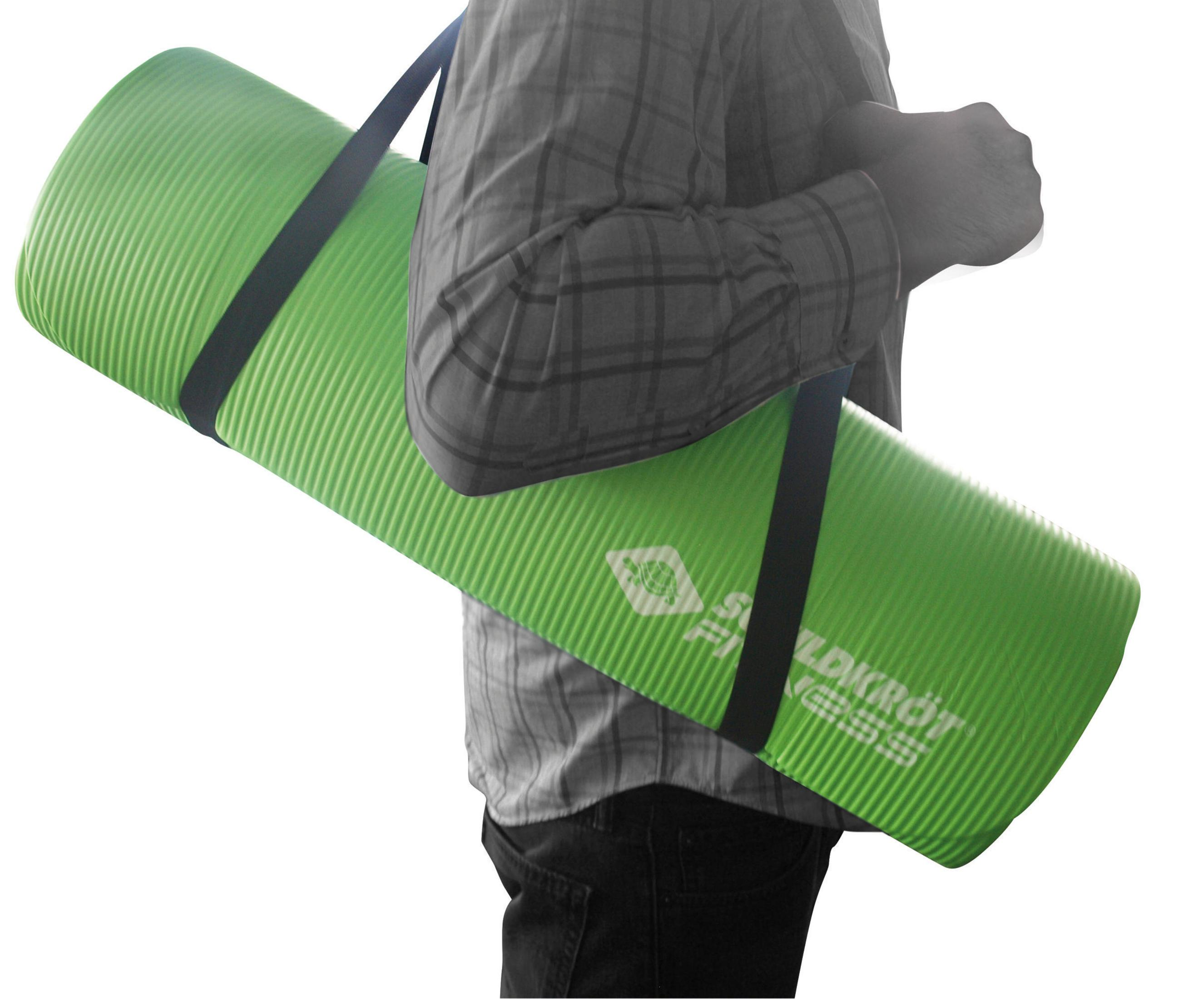 Person trägt gerollte grüne Yogamatte mit schwarzen Trägern, graues Hemd, Jeans.