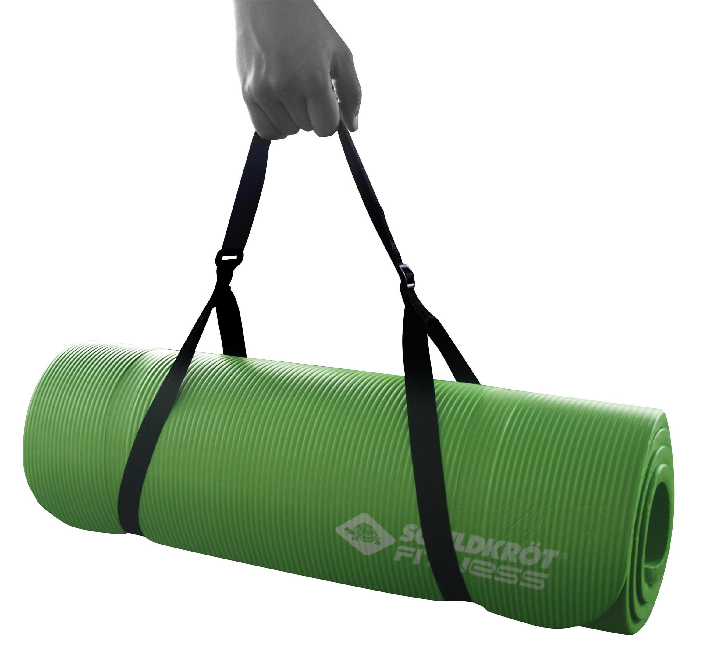 Eine grüne, gerollte Yogamatte wird von einer Hand mit schwarzen Trägern gehalten.