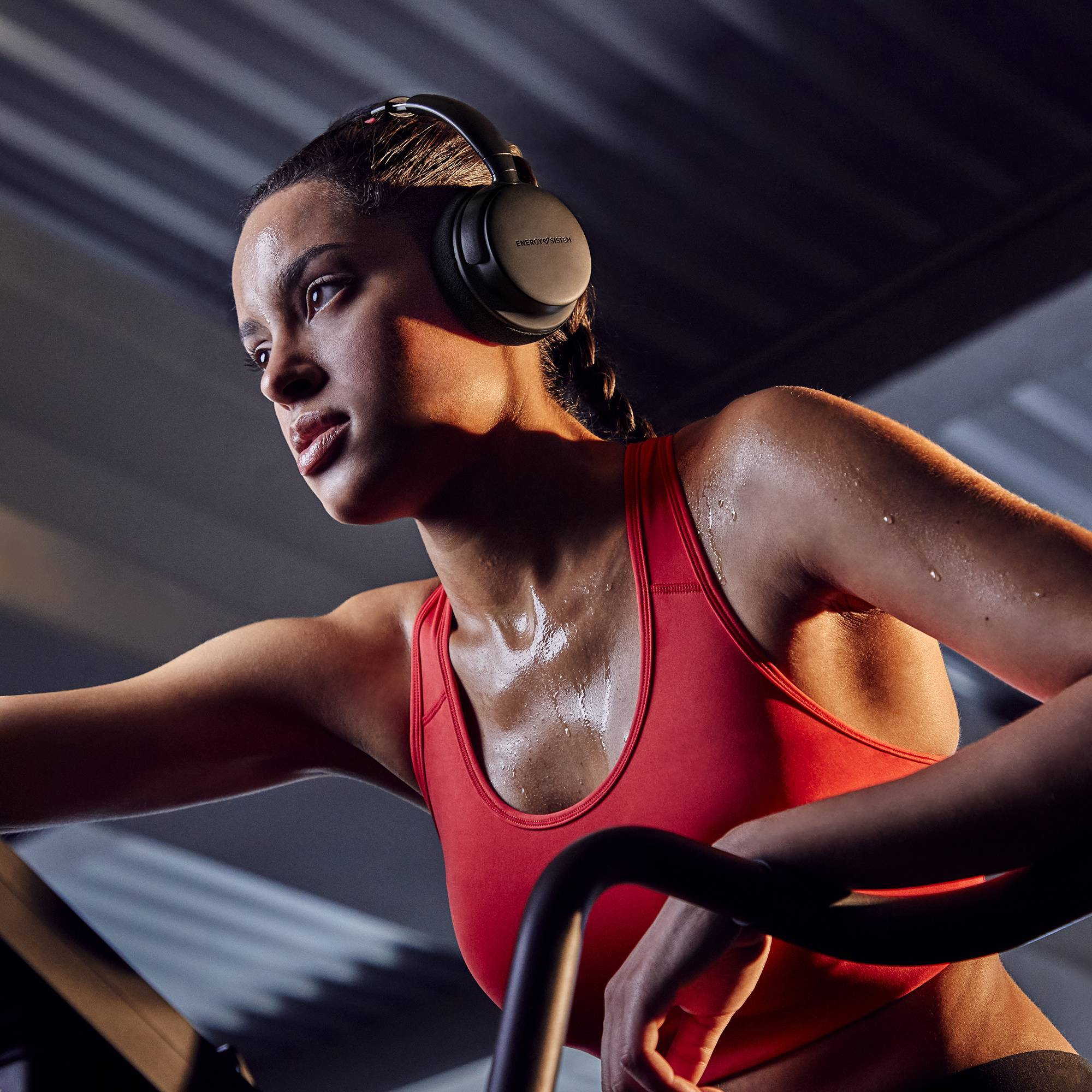 Kobieta w czerwonym staniku sportowym w czarnych słuchawkach, pocąca się podczas ćwiczeń.