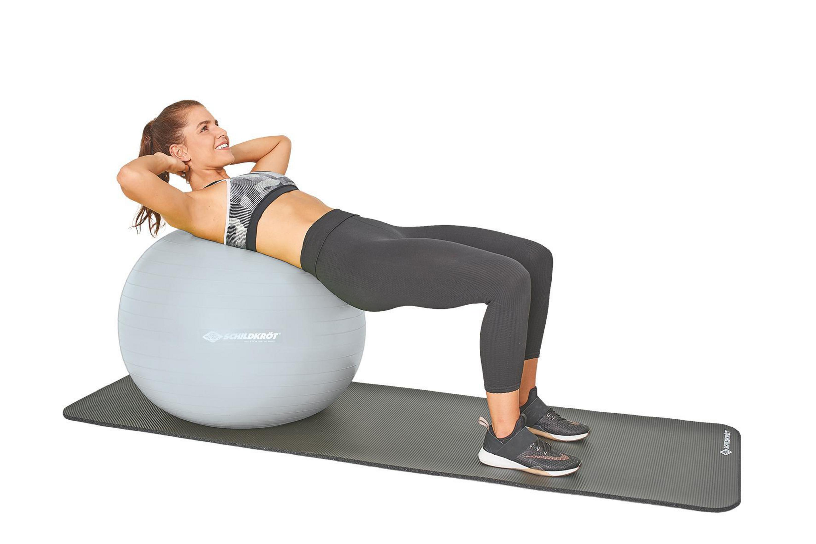 Eine Frau macht Sit-ups auf einer grauen Matte mit einem Gymnastikball.