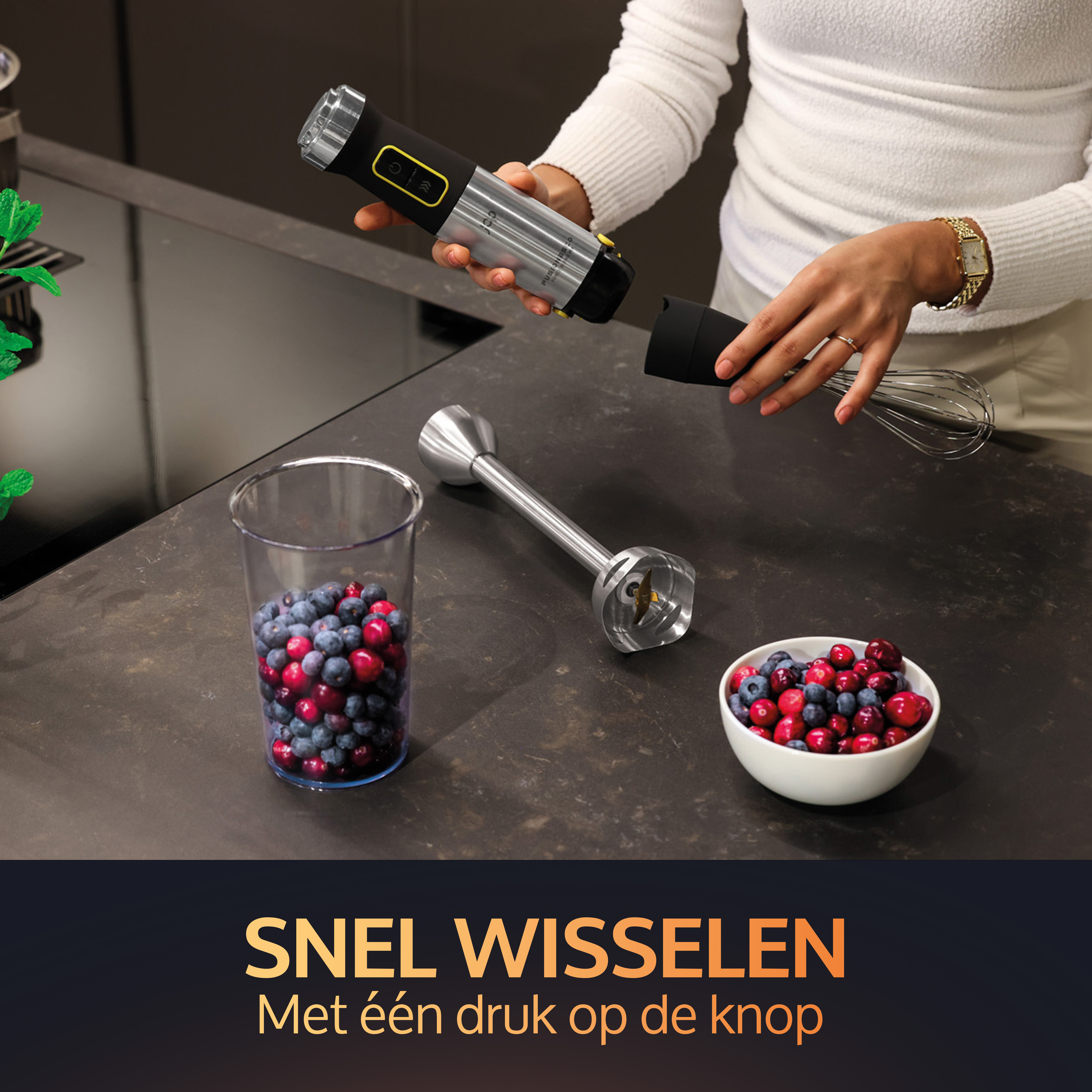 A hand blender being assembled with a cup of blueberries and a bowl of cranberries.