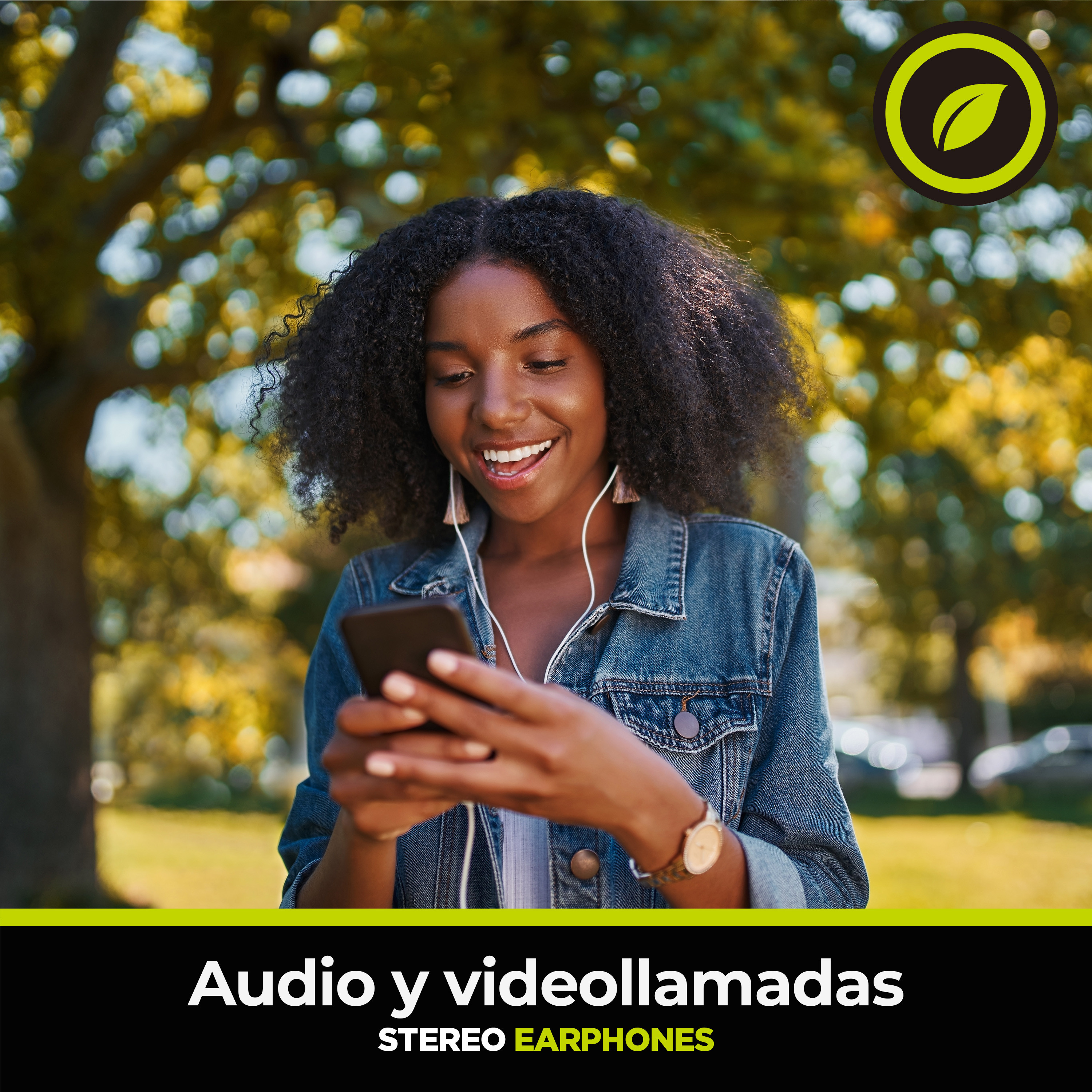 Una donna nera sorridente tiene in mano un telefono con auricolari in un parco, con un logo verde.
