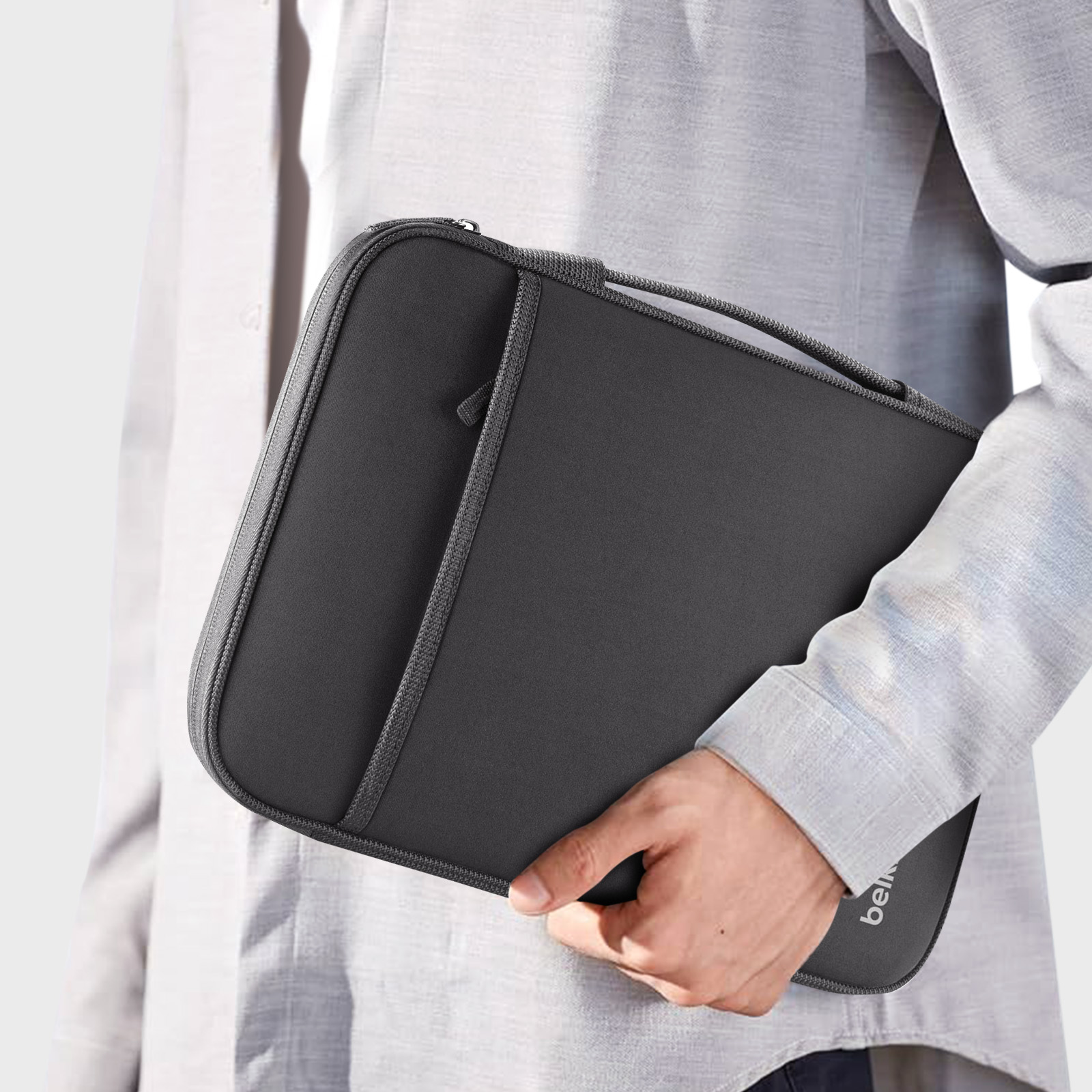Persona che tiene una custodia nera per laptop. La custodia ha una cerniera e una tasca. Belkin è stampato.
