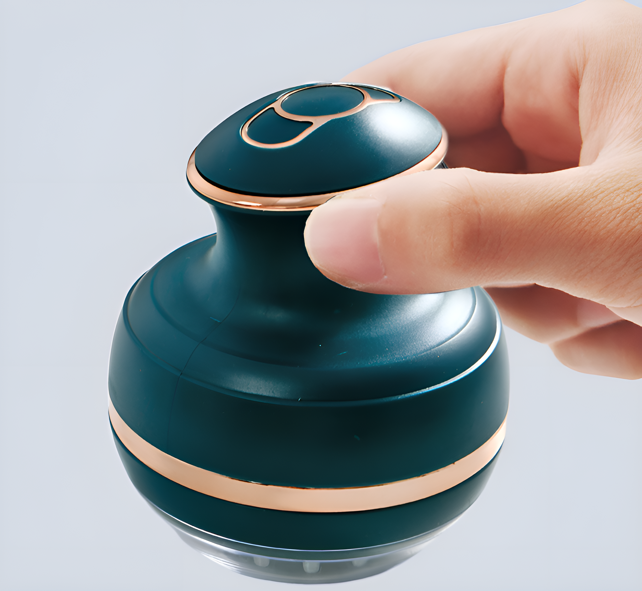 Eine Hand, die ein teal-goldenes Kopfmassagegerät mit kreisförmigem Design hält.