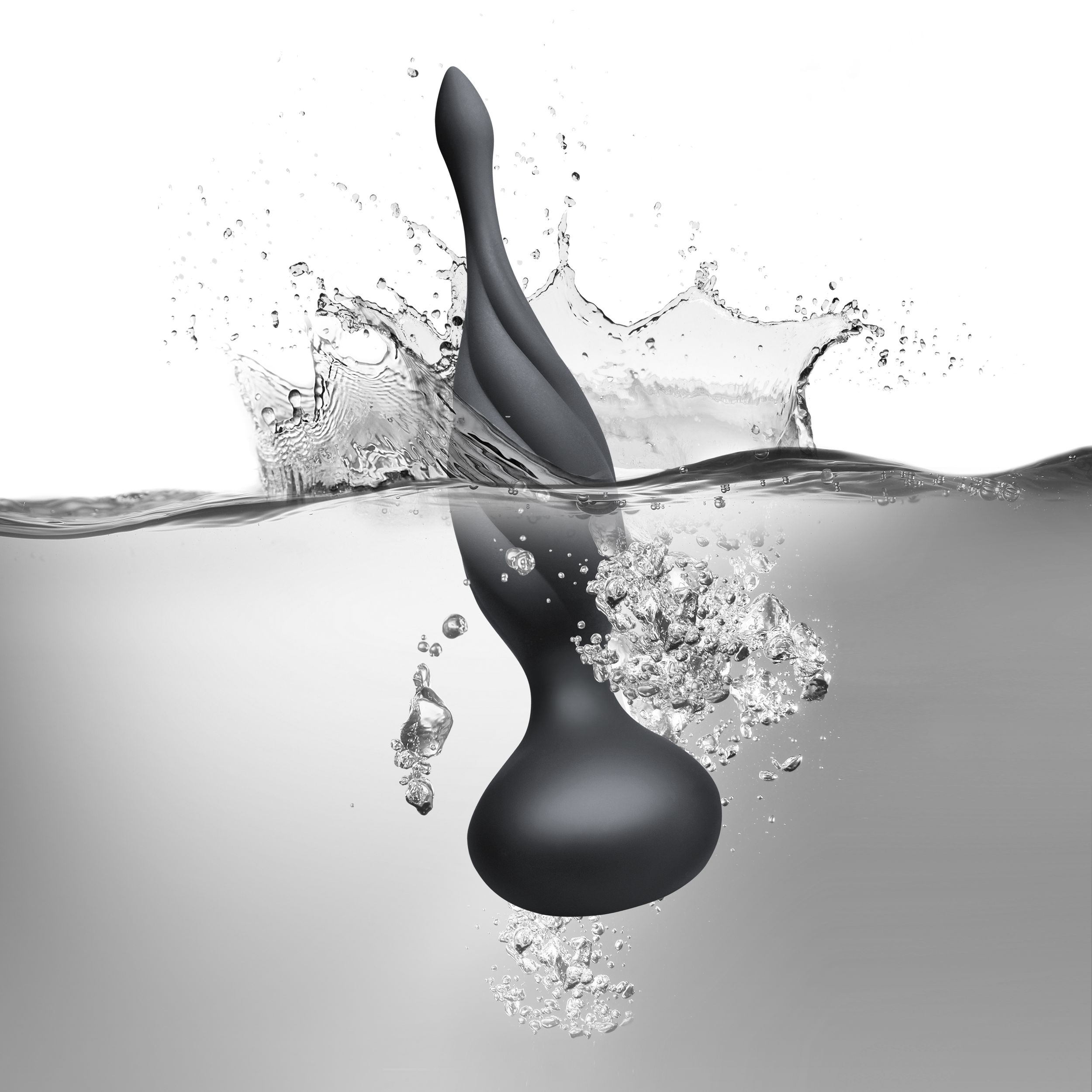 Un juguete sexual negro y curvado sumergido en agua, con salpicaduras y burbujas. El fondo es blanco.