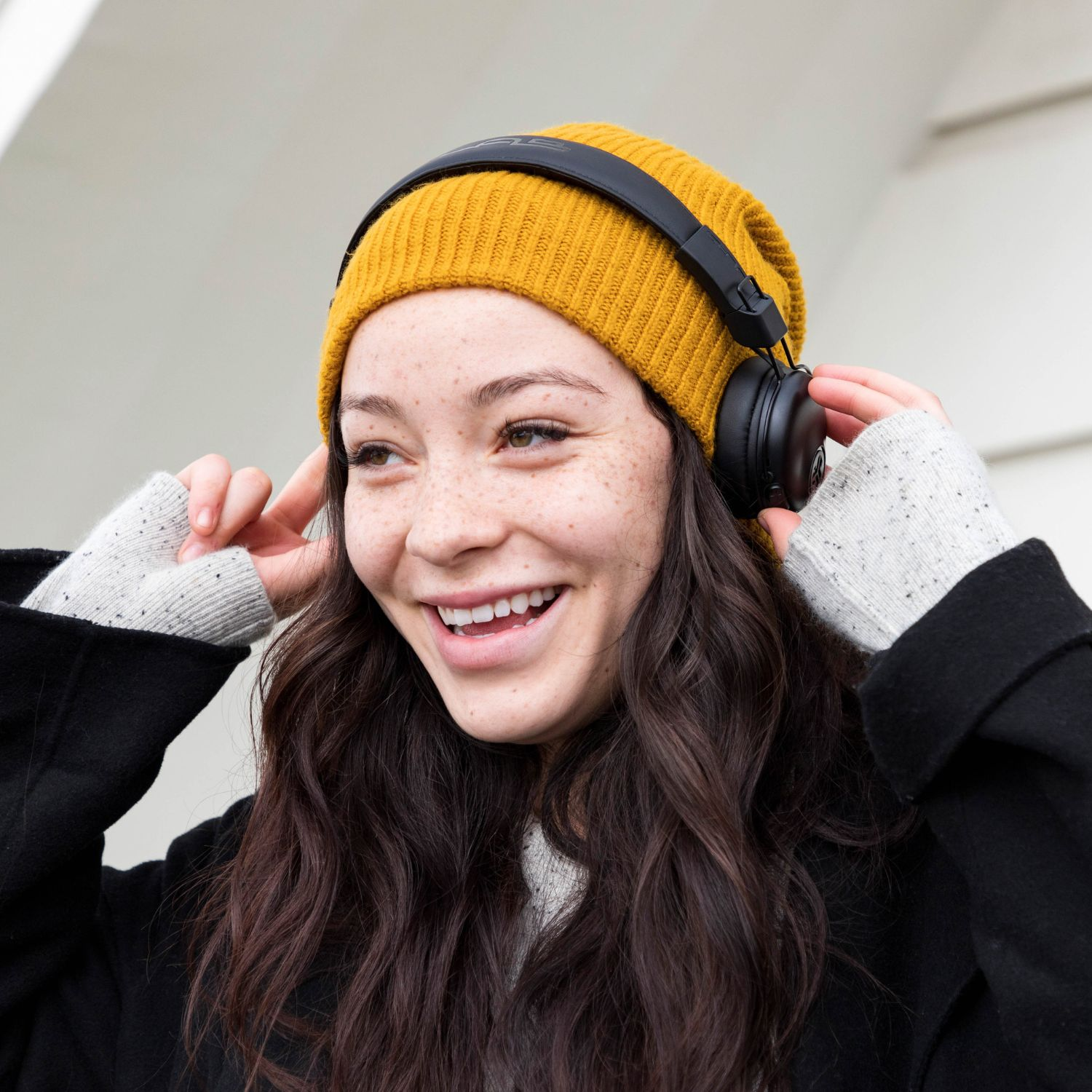 Una mujer sonriente con gorro amarillo y auriculares, al aire libre, luz natural.