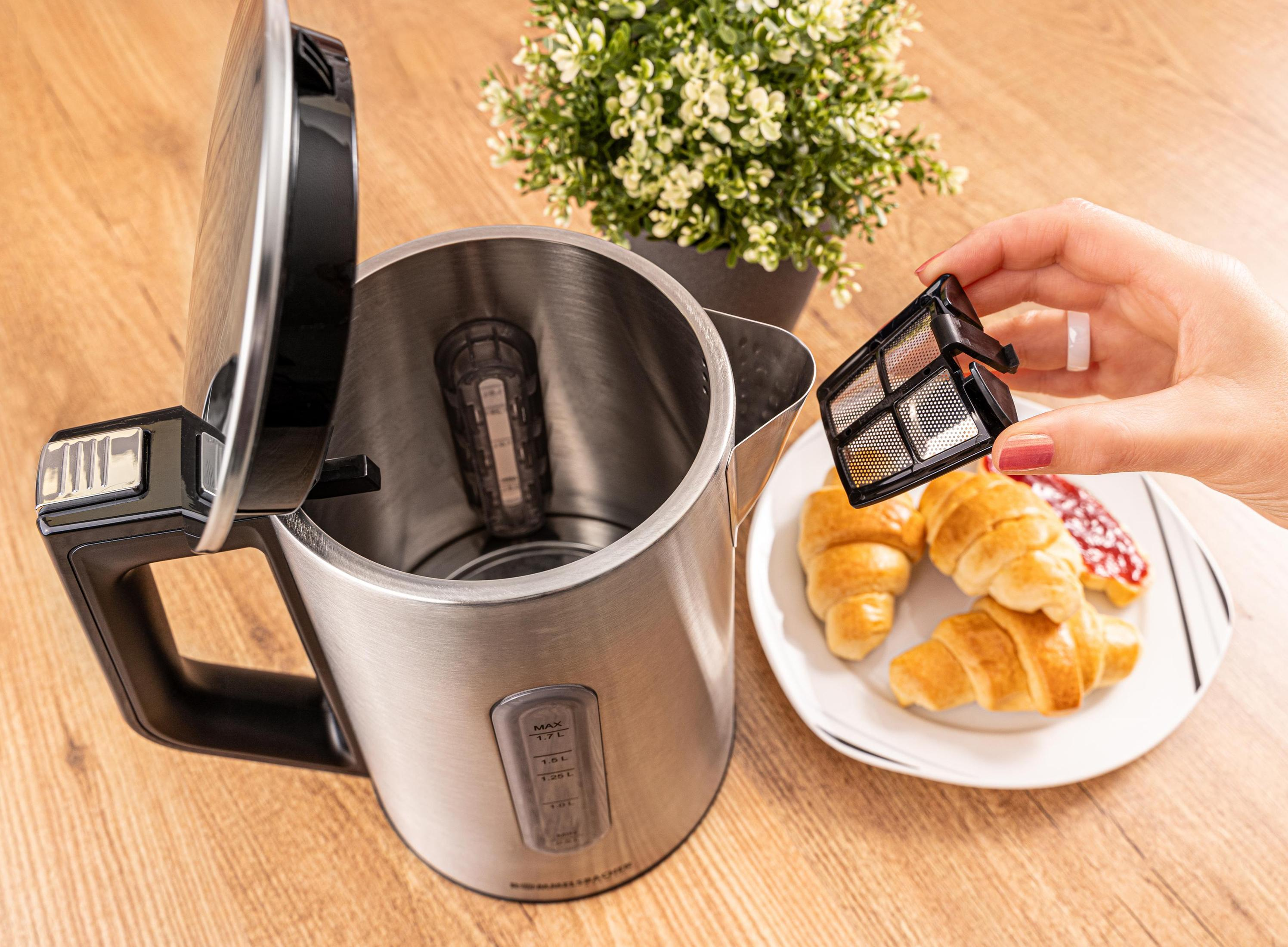 Ręka osoby trzymająca filtr z czajnika, obok jedzenia na drewnianej powierzchni.