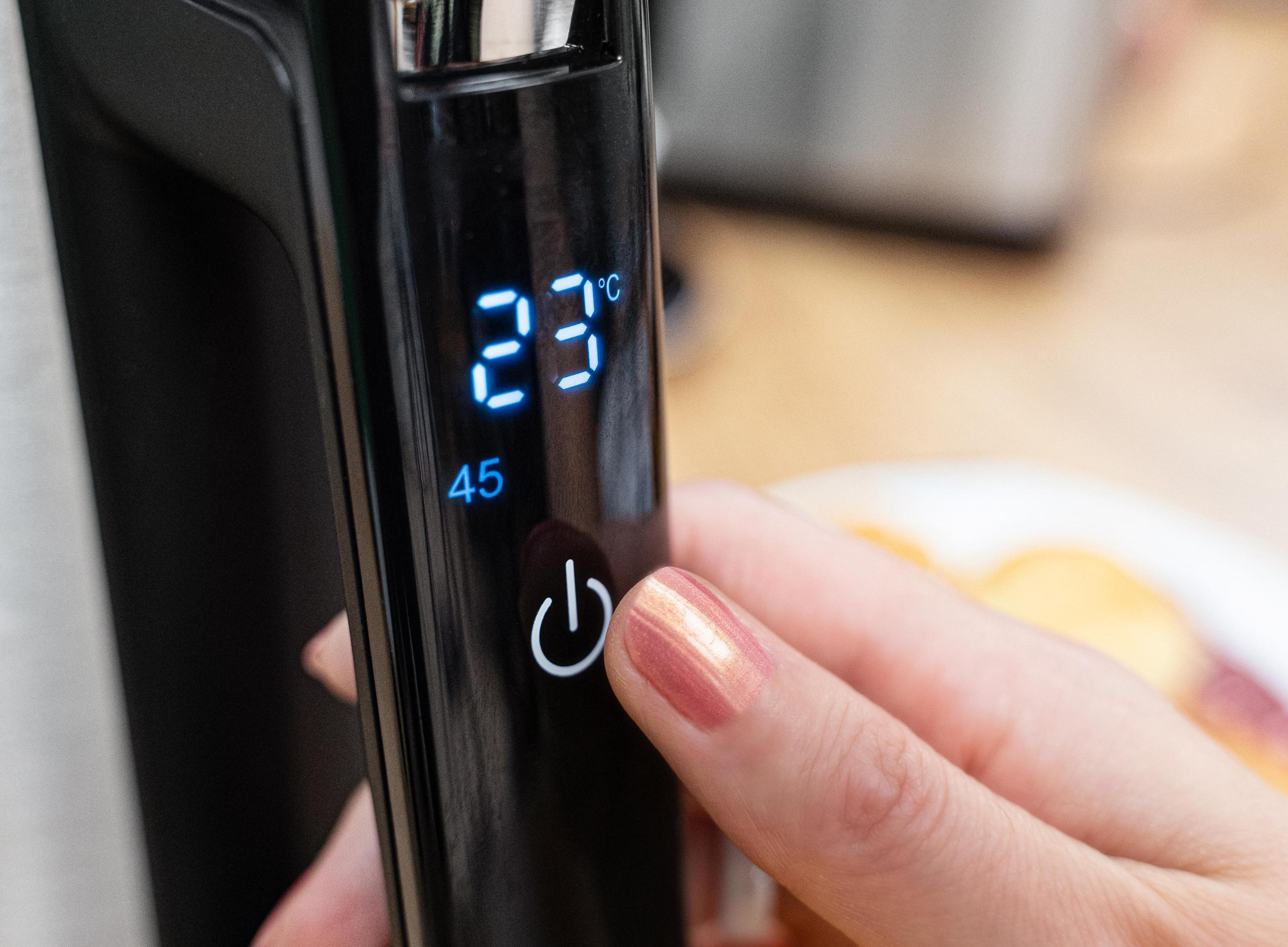 Zbliżenie ekranu urządzenia pokazującego 23°C. Palec naciska przycisk zasilania.