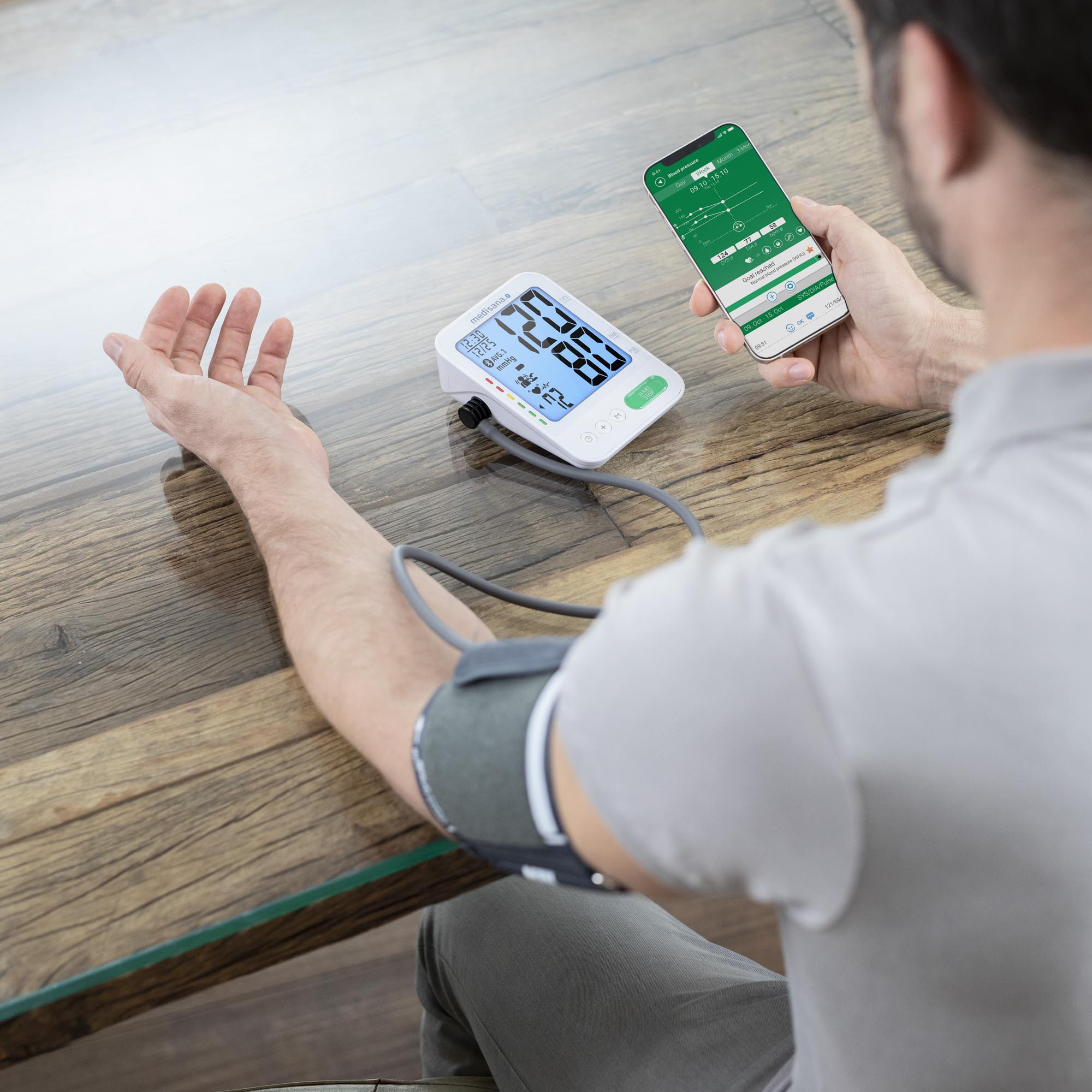 Mężczyzna używający monitora ciśnienia krwi na ramieniu, sprawdzający wyniki na podłączonym smartfonie.