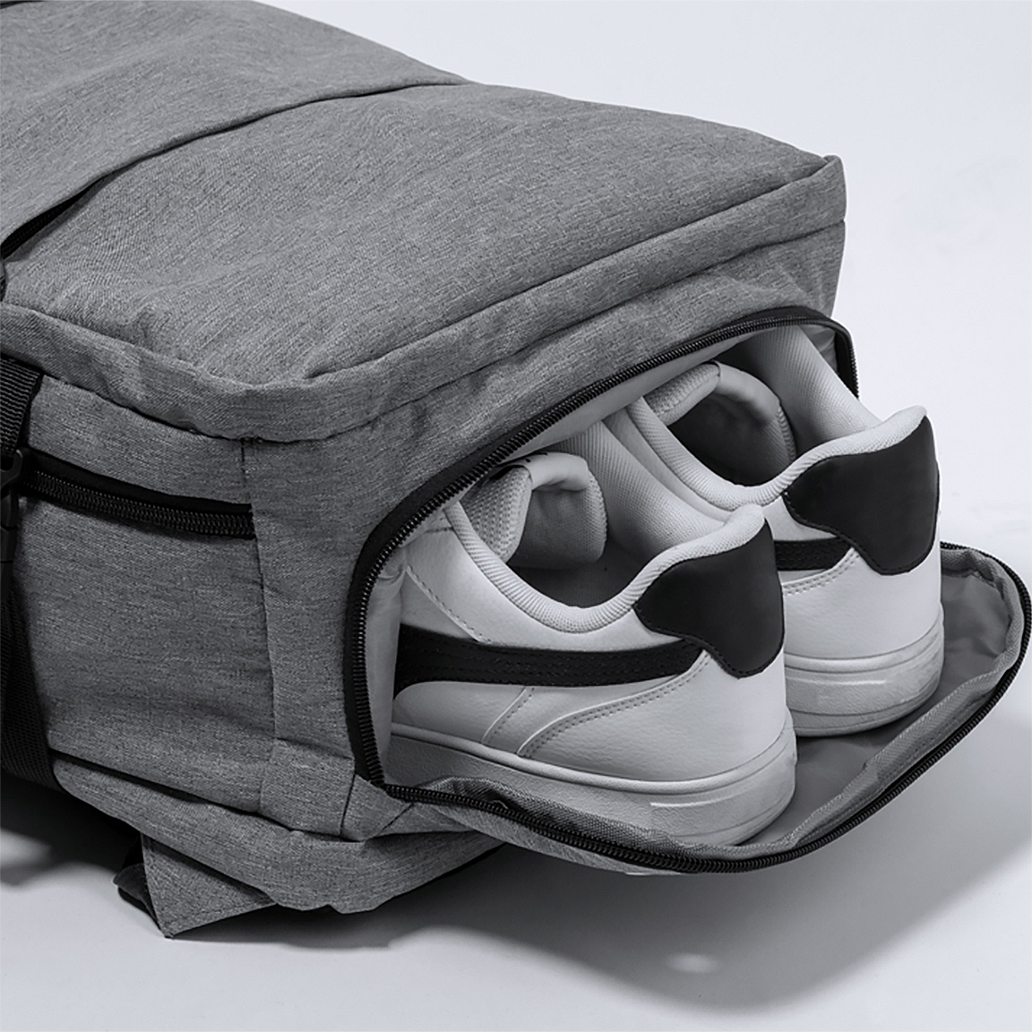 Una mochila gris con un compartimento para zapatos abierto. Dos zapatillas blancas y negras están dentro.