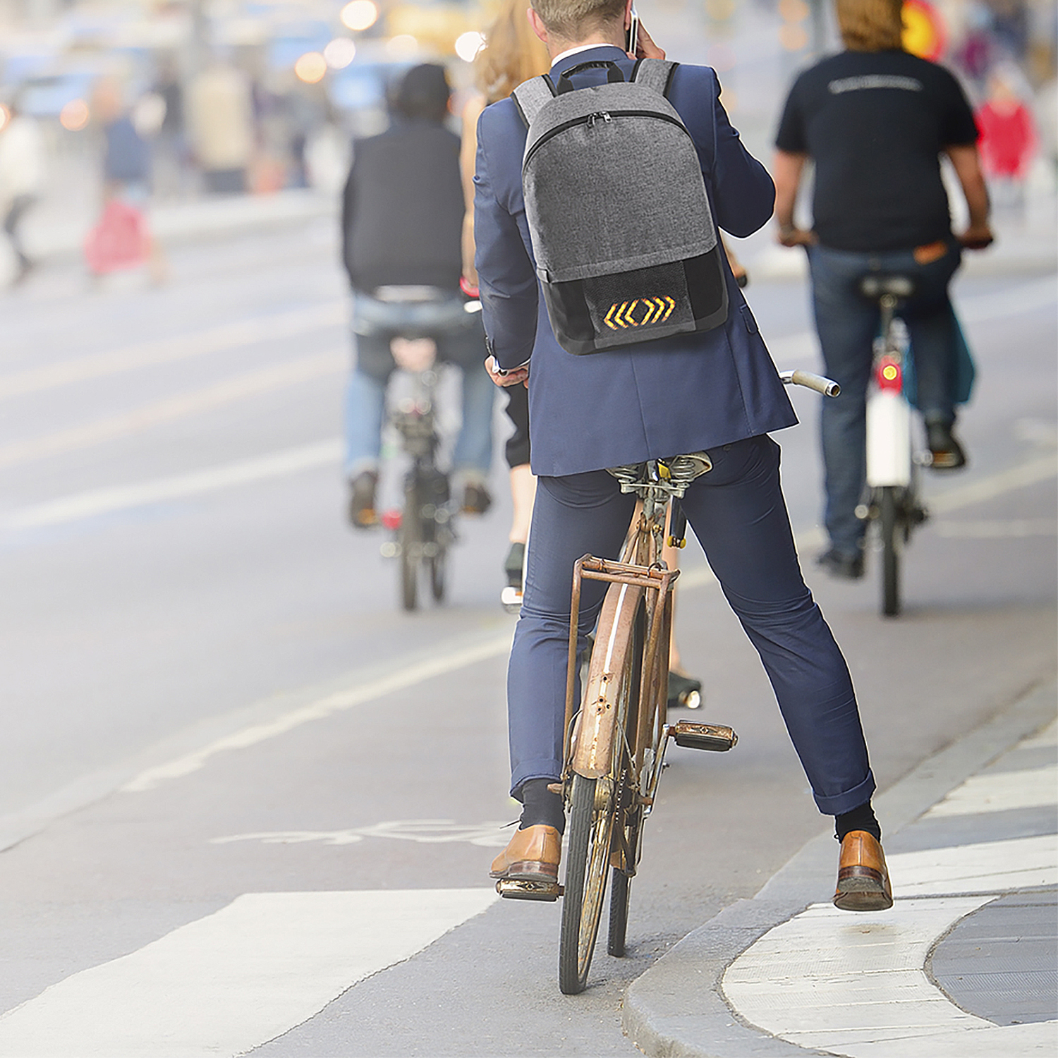 Uomo in bicicletta con zaino, parla al telefono, in una città.