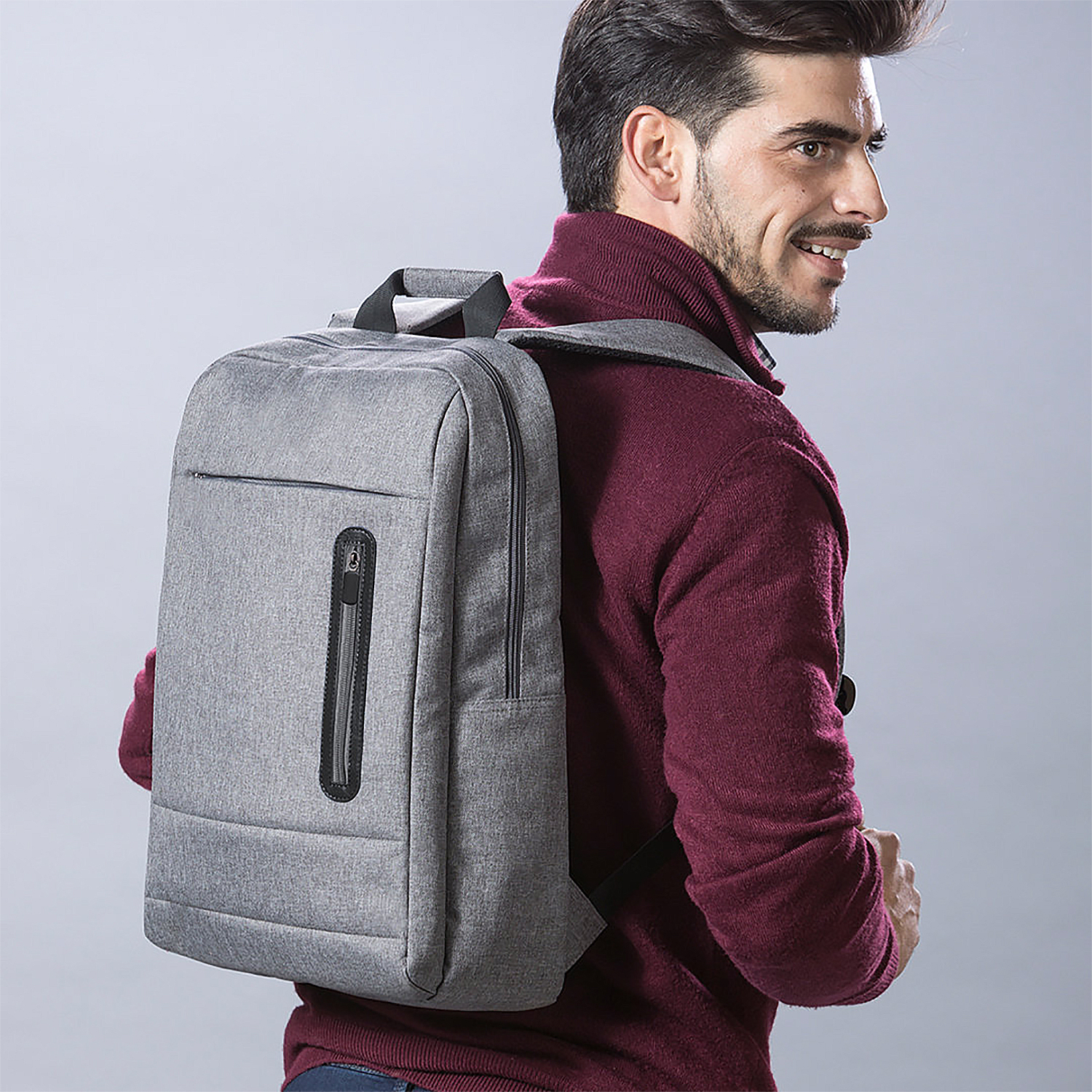 Uomo con zaino grigio e maglione bordeaux, sorridente, guarda a sinistra.
