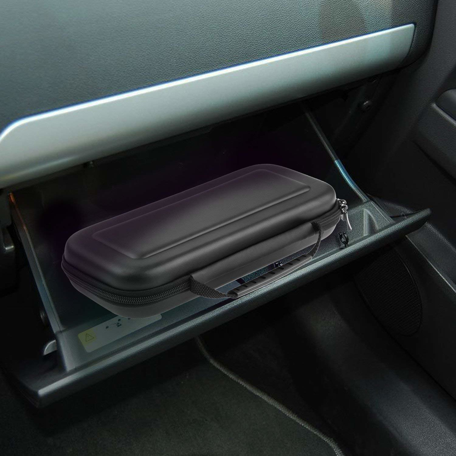 Ein schwarzes Hartschalenetui mit Reißverschluss im Handschuhfach eines Autos. Das Etui ist rechteckig.