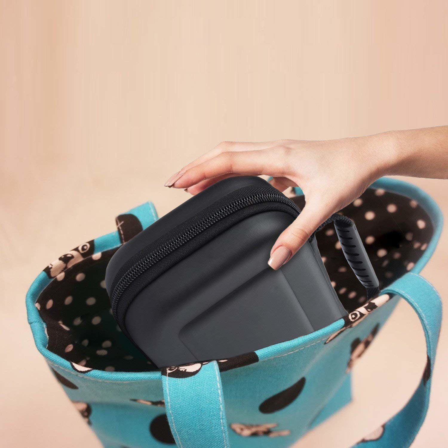 Eine Hand zieht einen schwarzen Koffer aus einer blauen Tragetasche mit schwarzen Punkten.