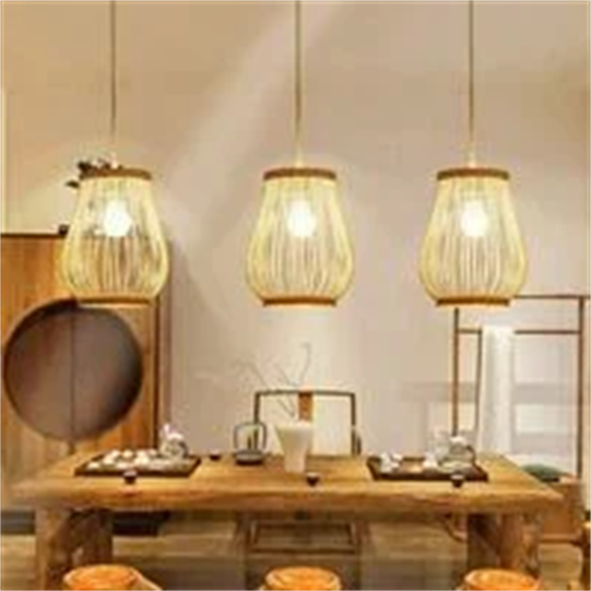 Drei Hängelampen mit gewebten Schirmen über einem Holztisch mit Tee-Arrangement. Im Hintergrund Holzmöbel.
