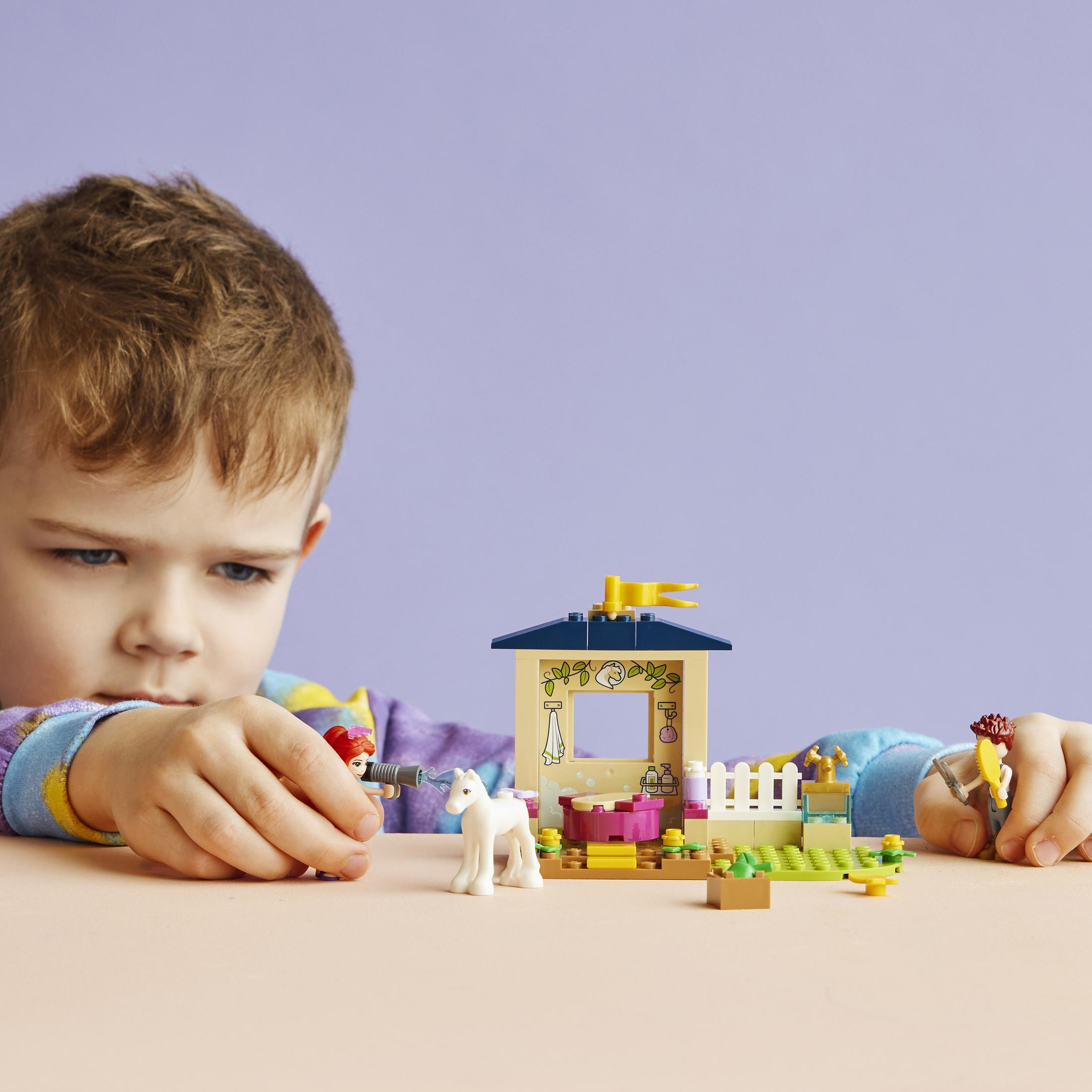 Een kind speelt met een Lego set met een huis en een paard.