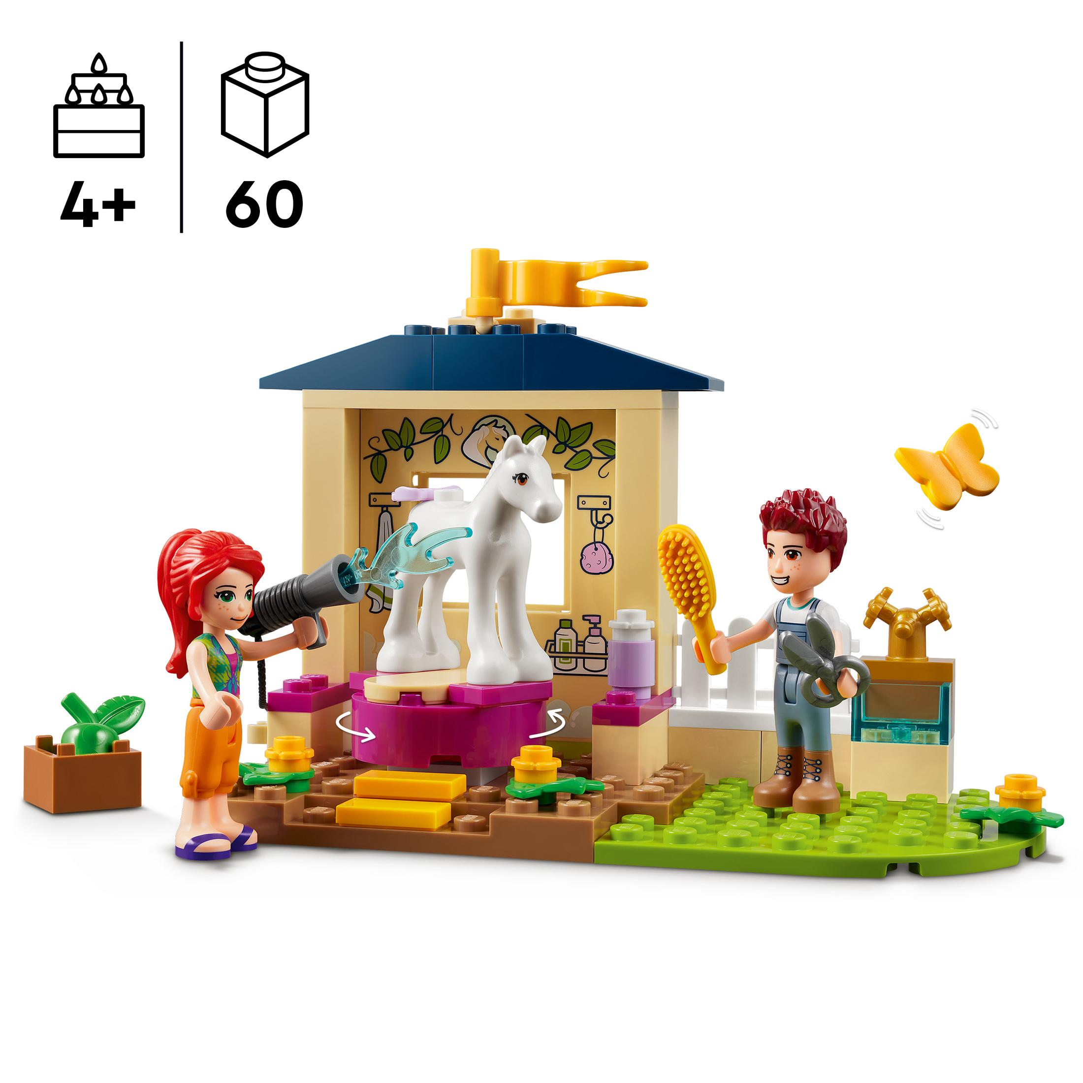 Lego set van een paard dat wordt gewassen door twee figuren in een stal met een vlinder en planten.