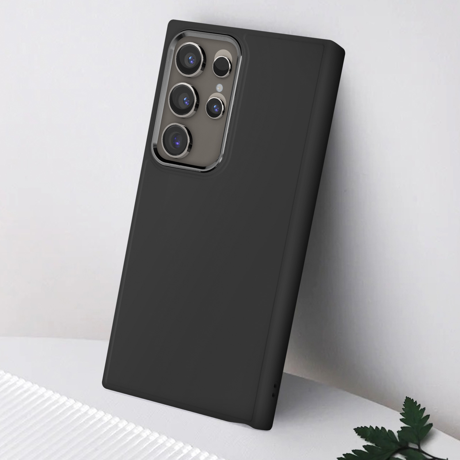 Custodia per telefono nera con un gruppo fotocamere su un tavolo bianco e una pianta verde.