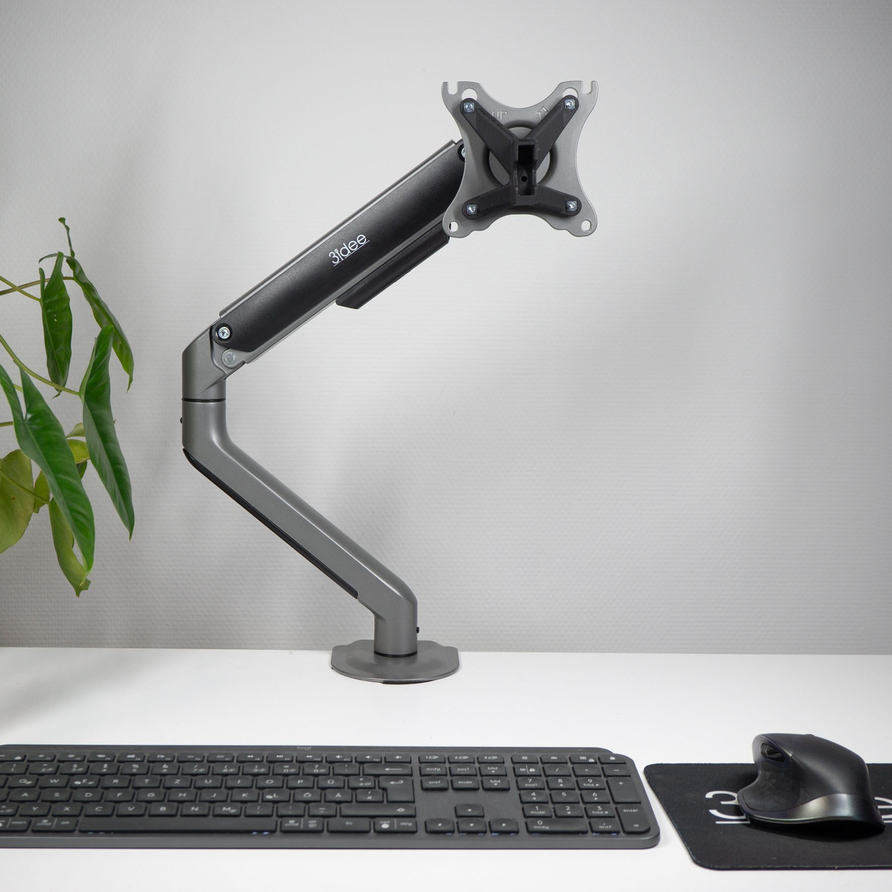Monitorarm mit Computerbildschirm, Tastatur, Maus und einer grünen Pflanze auf einem weißen Schreibtisch.