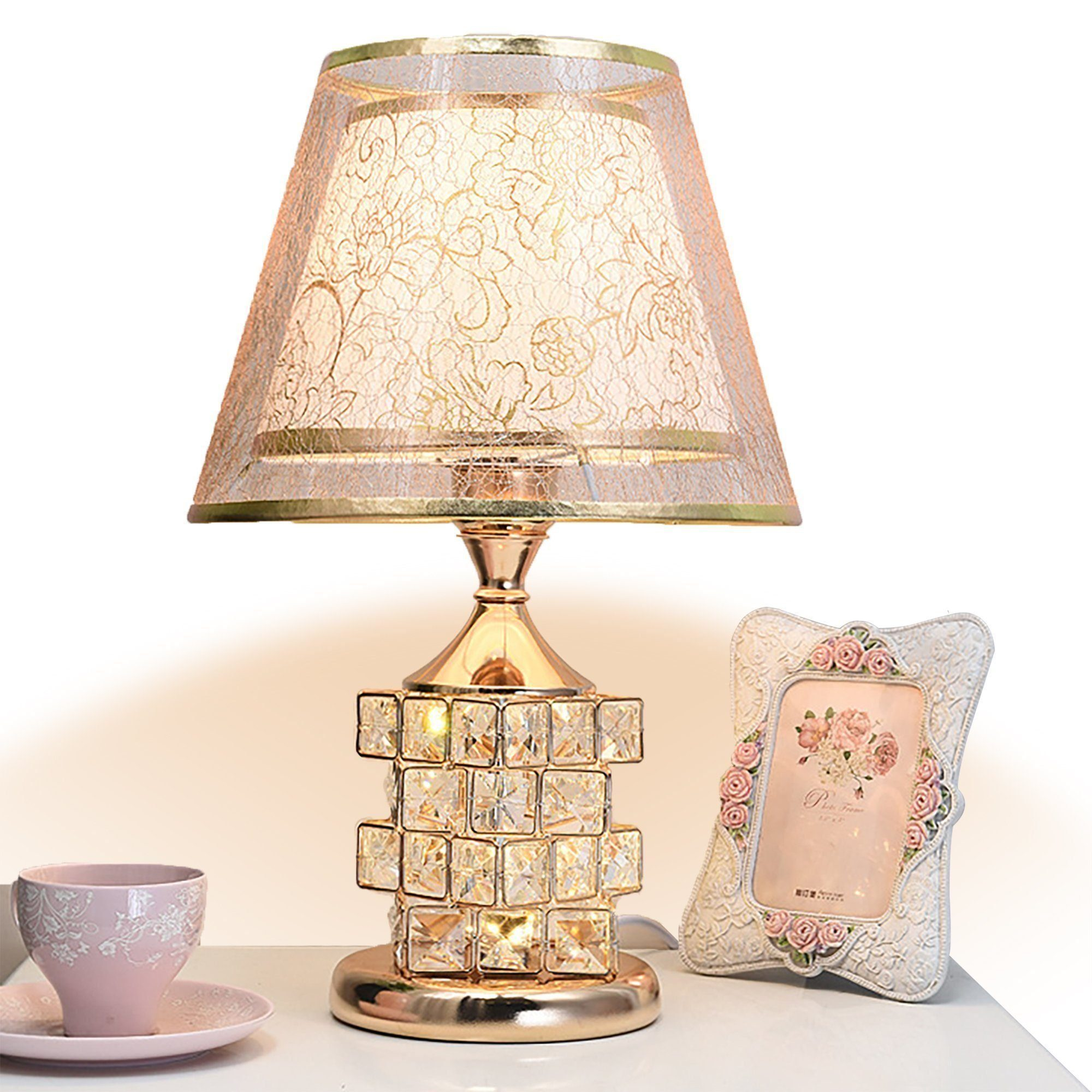 Eine dekorative Tischlampe mit Lampenschirm, Kristallfuß und gerahmtem Bild.