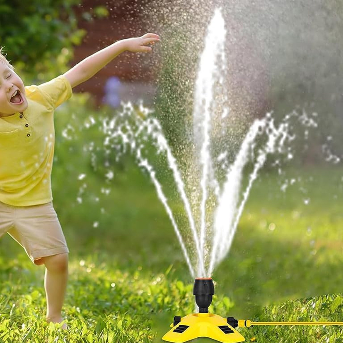 Junger Junge spielt in einem Garten mit einem gelben Rasensprenger, der Wasser nach oben spritzt.