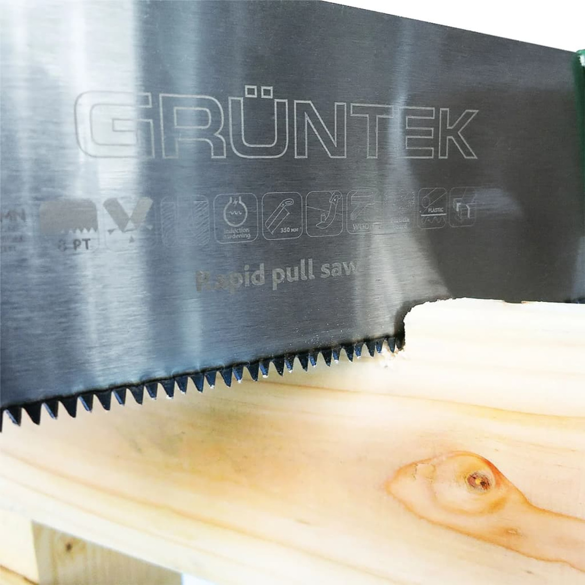 Nahaufnahme einer Handsäge, die Holz schneidet. Die Säge ist silberfarben mit dem Wort 'GRÜNTEK'.