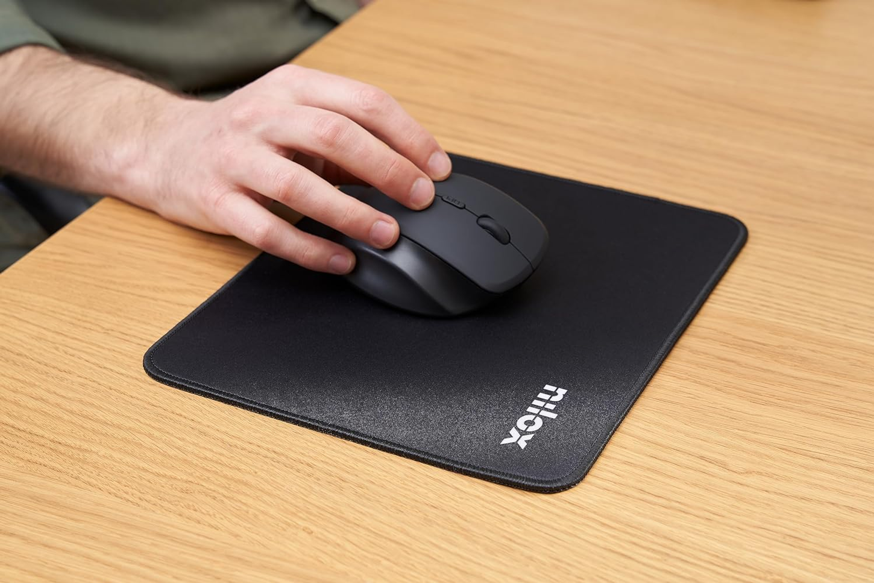 Een hand die een grijze muis gebruikt op een zwart muismatje met het 'nilox'-logo zichtbaar.