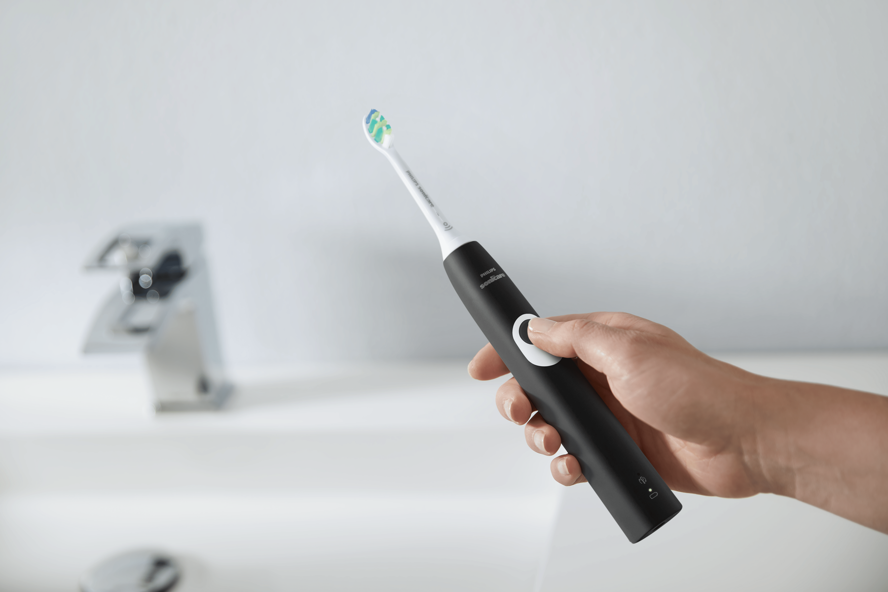 Cepillo de dientes eléctrico negro en una mano. Cerca de un lavabo y grifo.