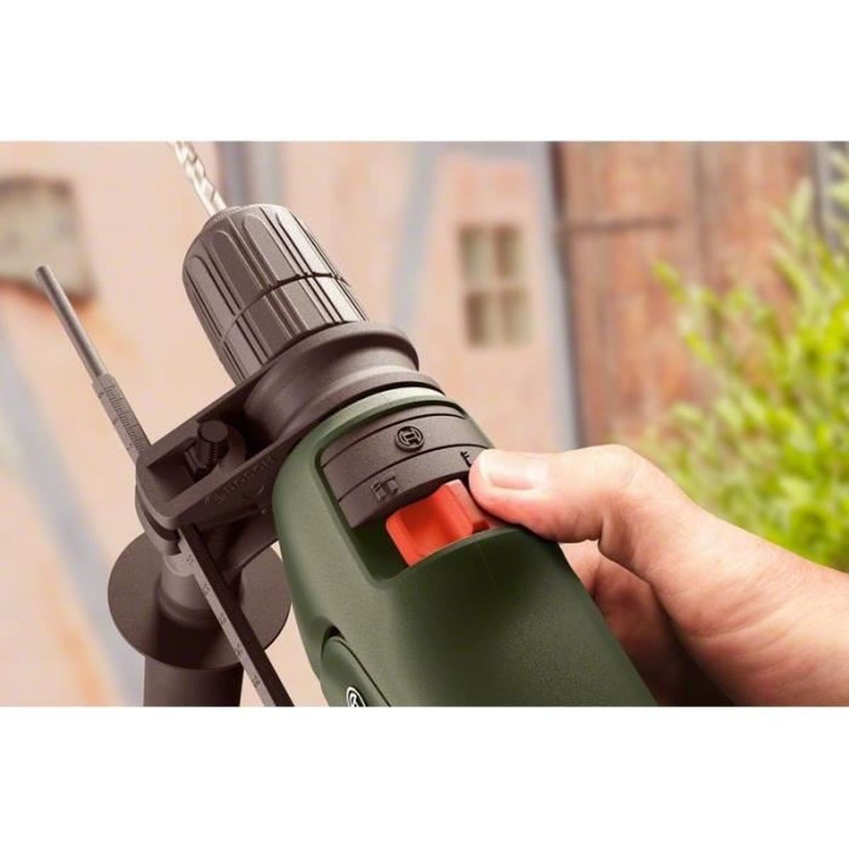 Mano presionando el botón en un taladro verde y negro con una broca extendida.