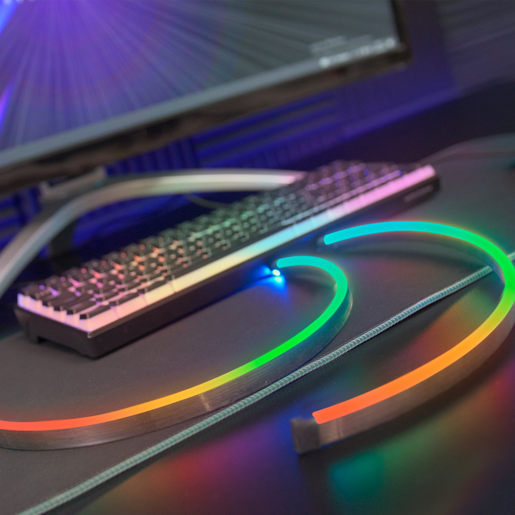Una configuración de escritorio con teclado, monitor y una tira de luz LED curva que brilla en varios colores.