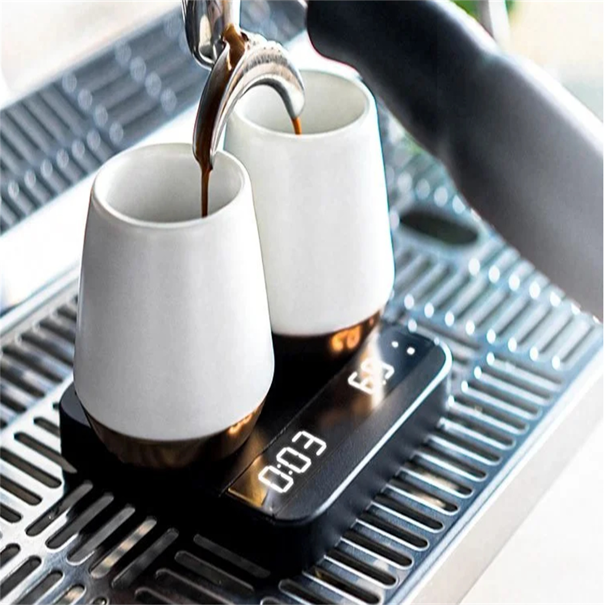 Espressomaschine brüht Kaffee in zwei weiße Tassen mit goldenen Böden, auf einer digitalen Waage.