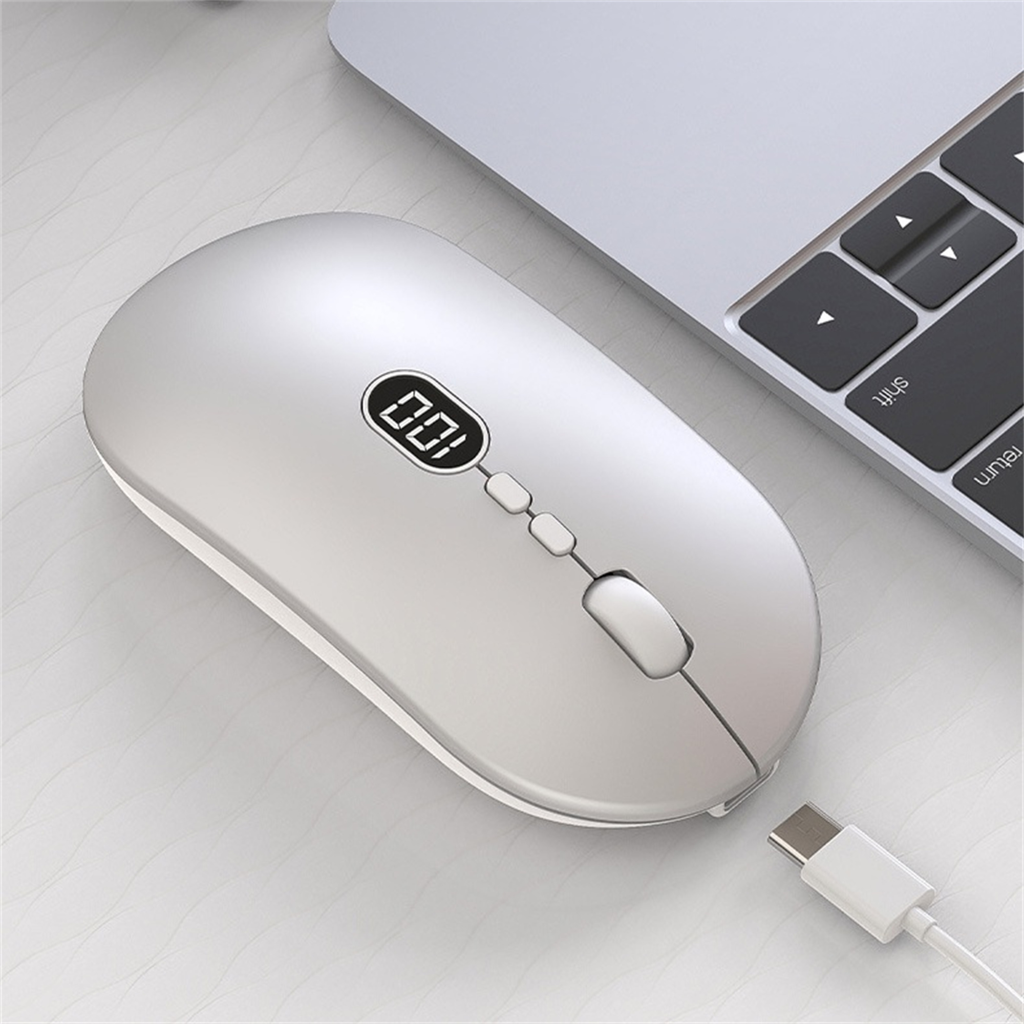 Silberne Computermaus mit kleinem Bildschirm, der '100' anzeigt. Ein Ladekabel ist eingesteckt.