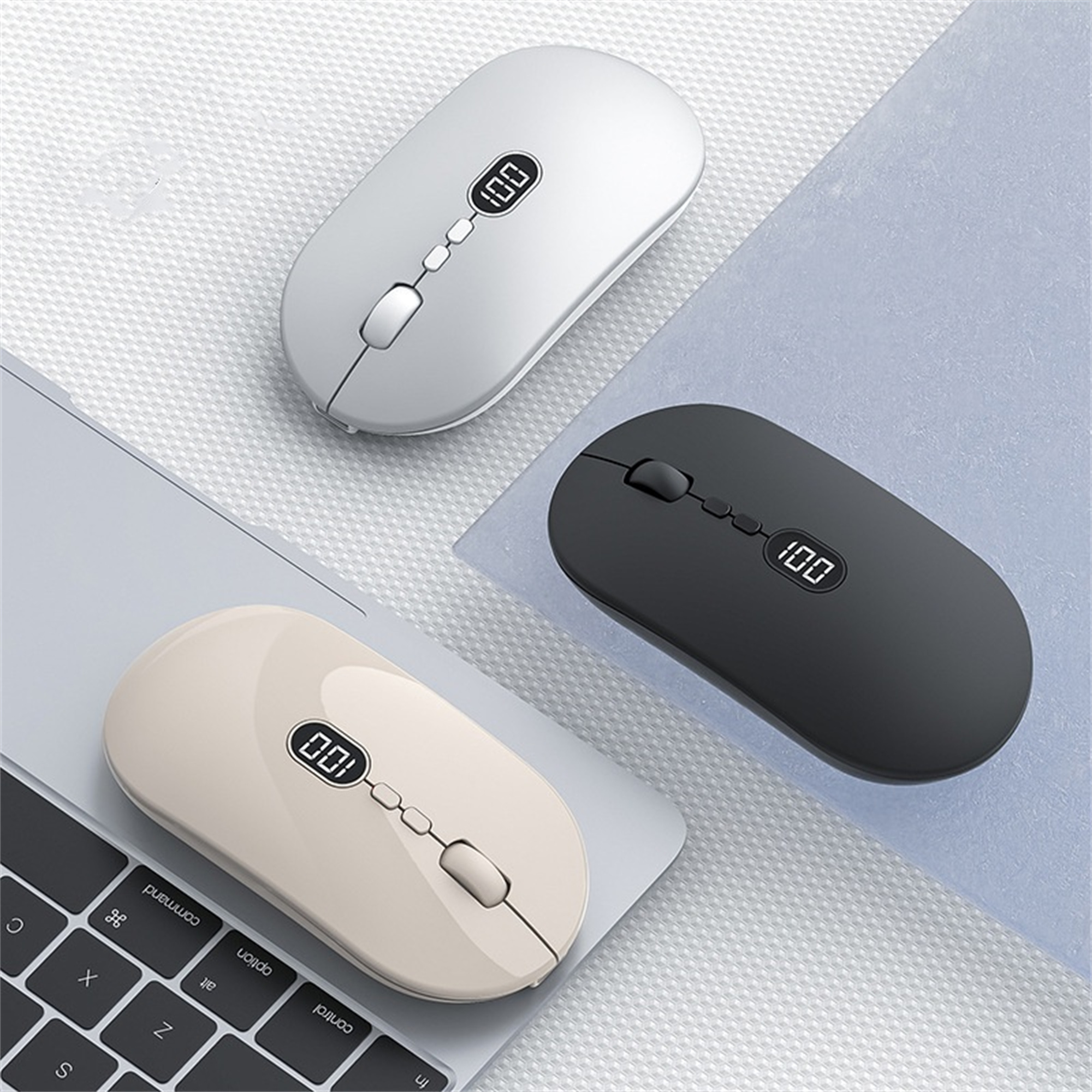 Drei kabellose Computermäuse: weiß, beige und schwarz auf einem Laptop.