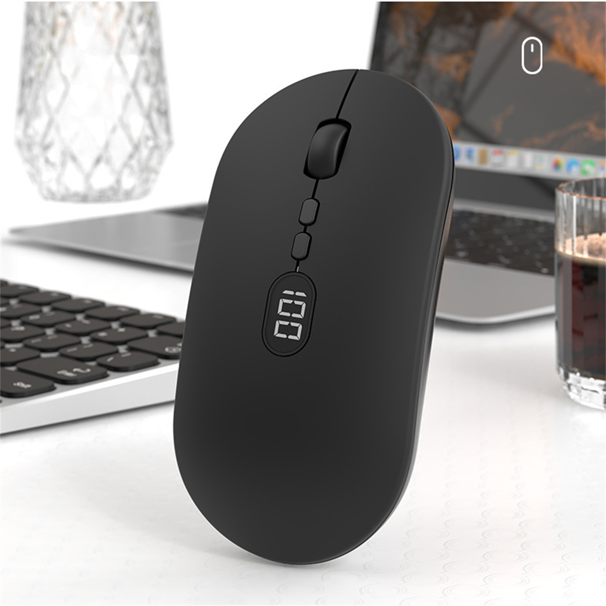 Schwarze kabellose Maus mit Anzeige '100'. Tastatur und Kaffeeglas im Hintergrund, weiße Oberfläche.