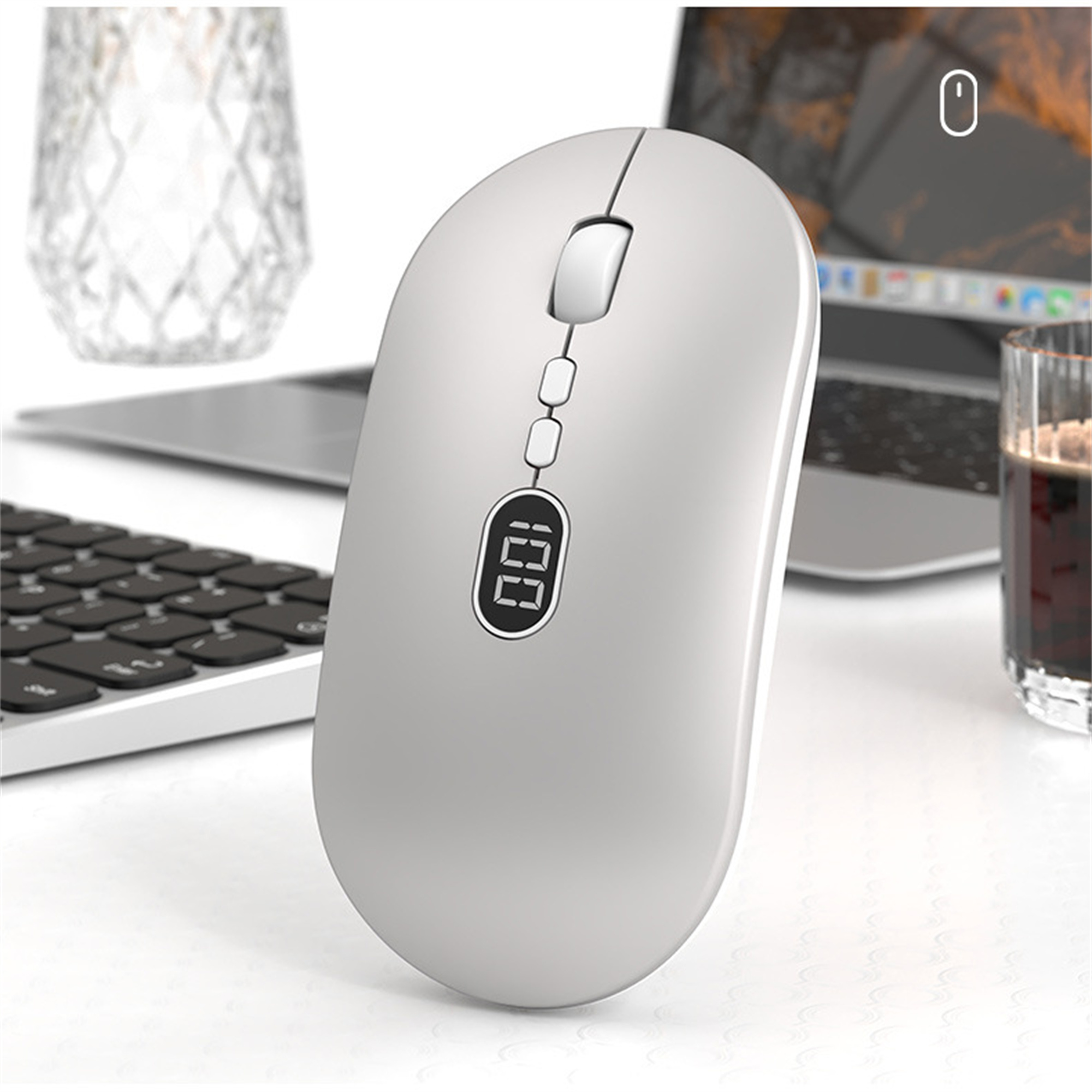 Eine weiße Maus mit Display. Sie liegt auf einem Schreibtisch, in der Nähe einer Tastatur und eines Glases.