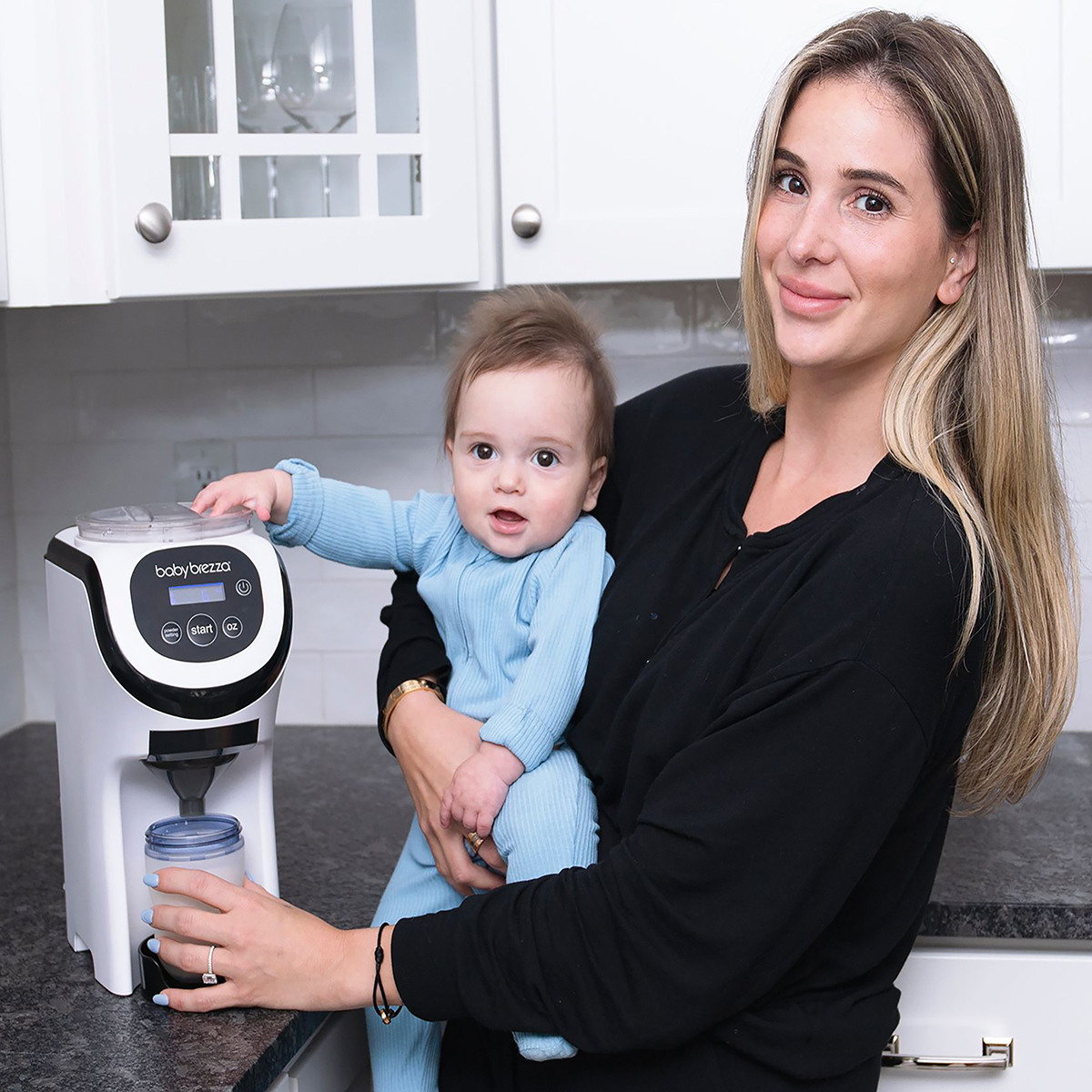 Eine Frau hält ein Baby und einen Babynahrungsbereiter in einer Küche.