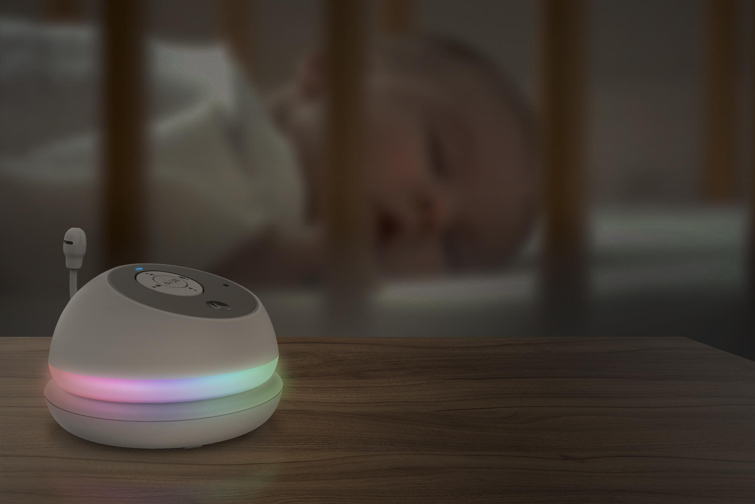 Baby monitor on a wooden table. A sleeping baby is blurred in the background.