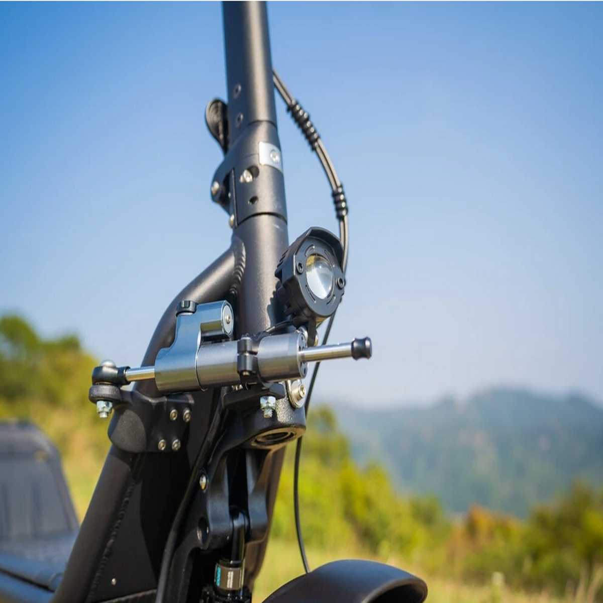 Primo piano della parte anteriore di un e-scooter con luce e sistema di sospensione, su uno sfondo panoramico.